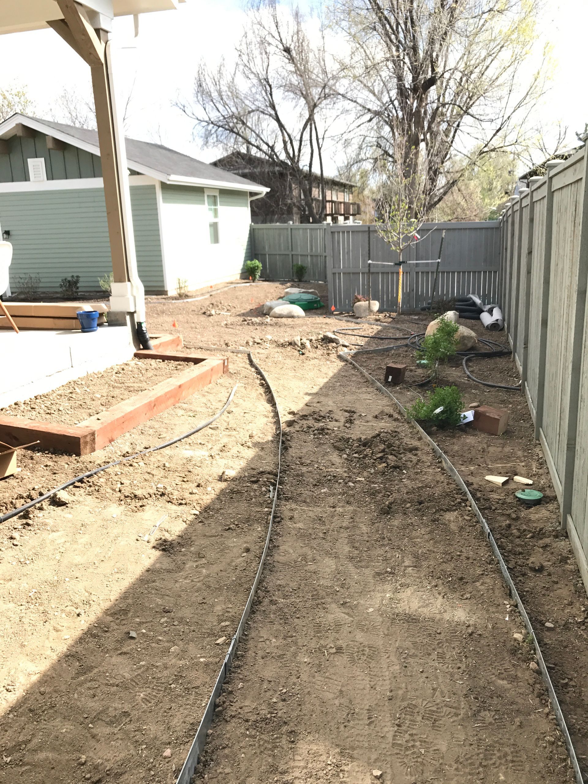 Backyard with dirt path, raised garden bed, gray fence, and a light green house.
