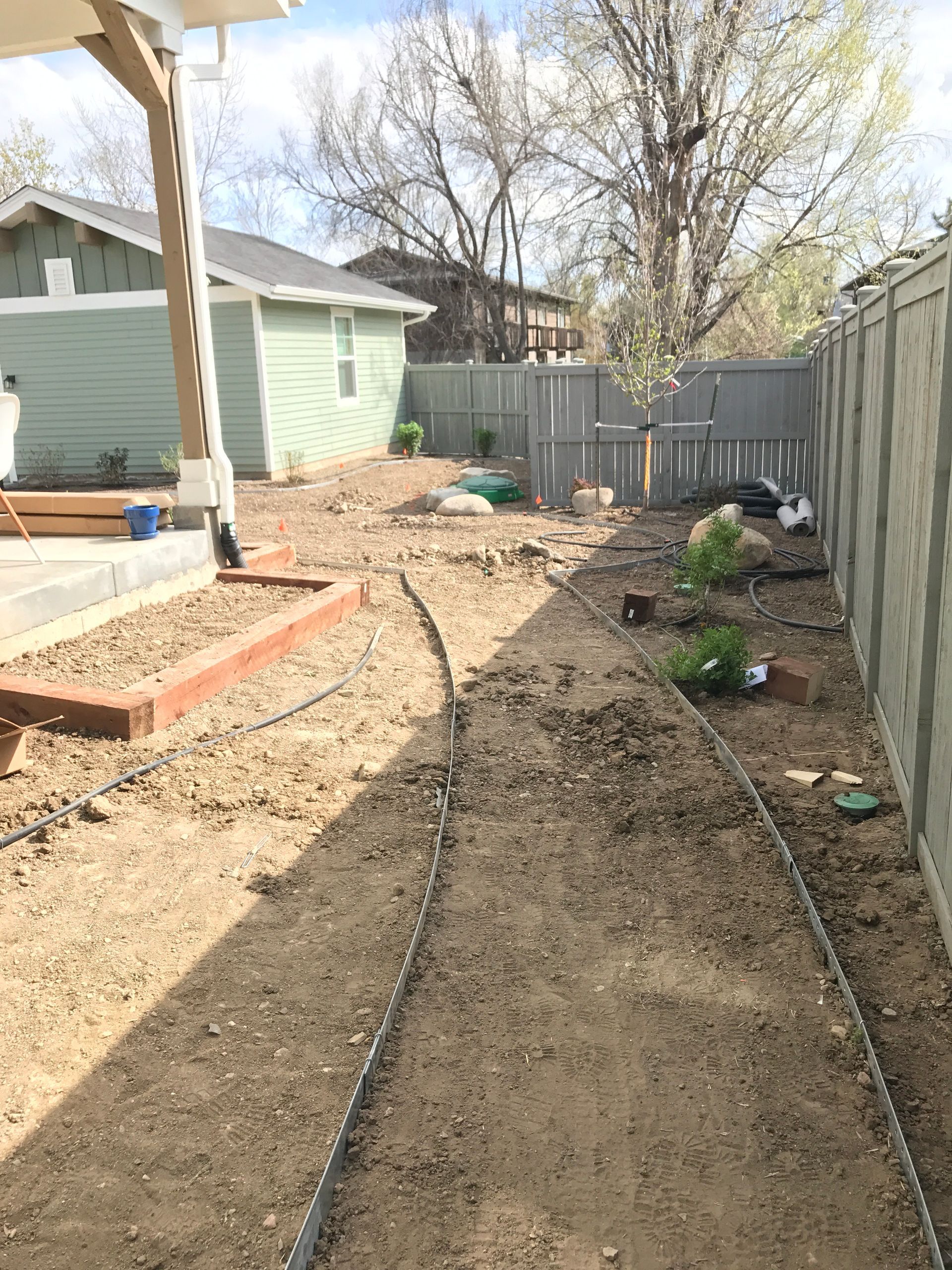 Backyard with a dirt path edged with metal, garden beds, and a fence.