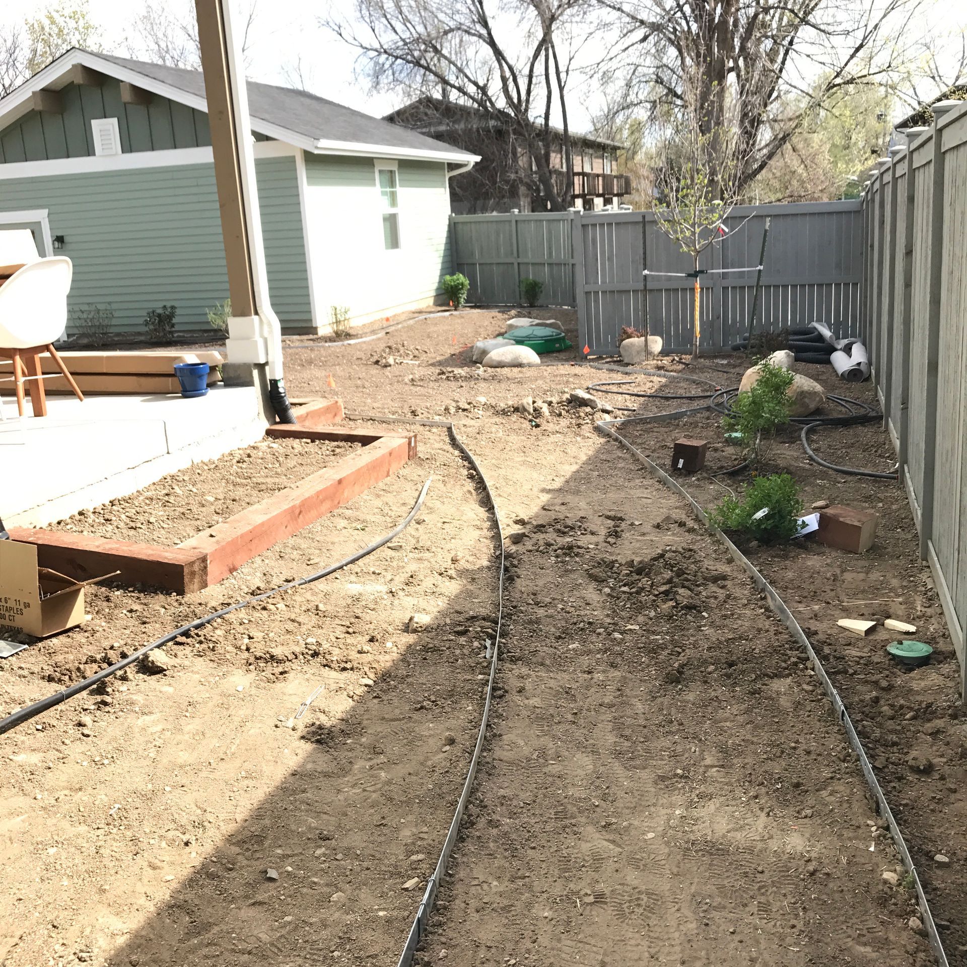 Backyard with dirt pathways, garden beds, and a green house.