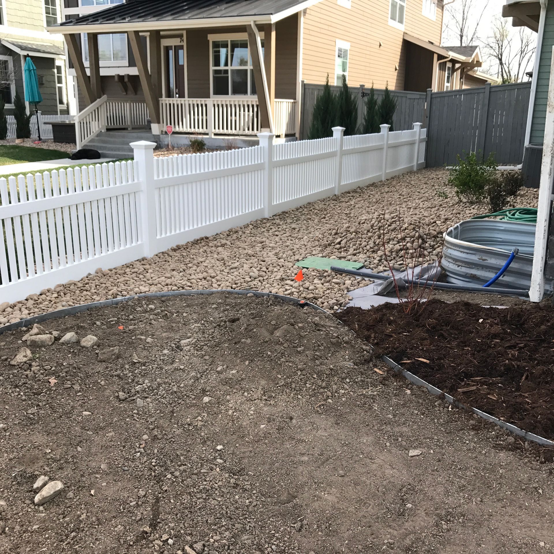 White picket fence alongside a gravel and mulch yard, in front of a house.