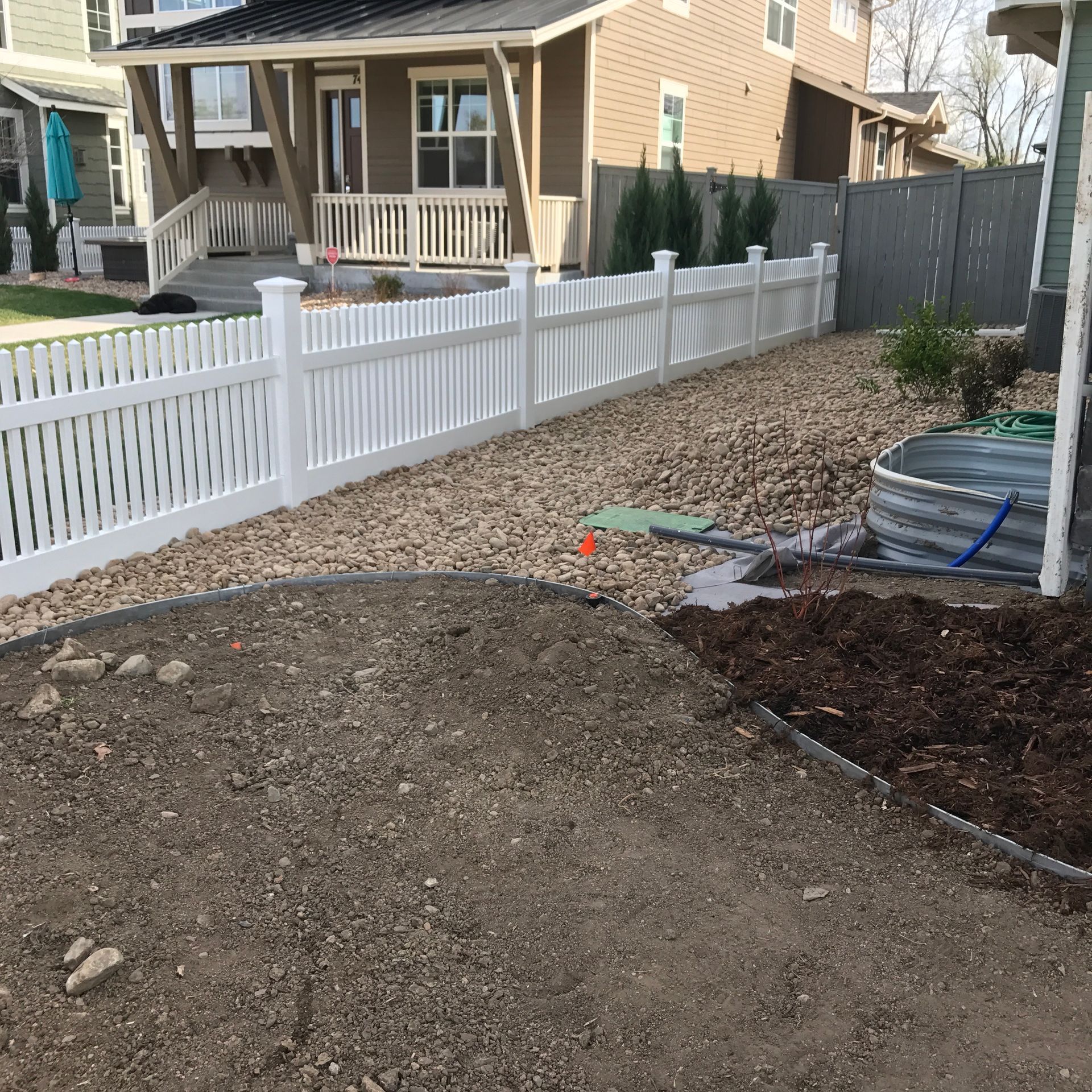 White picket fence along a residential property with gravel and dirt landscaping.