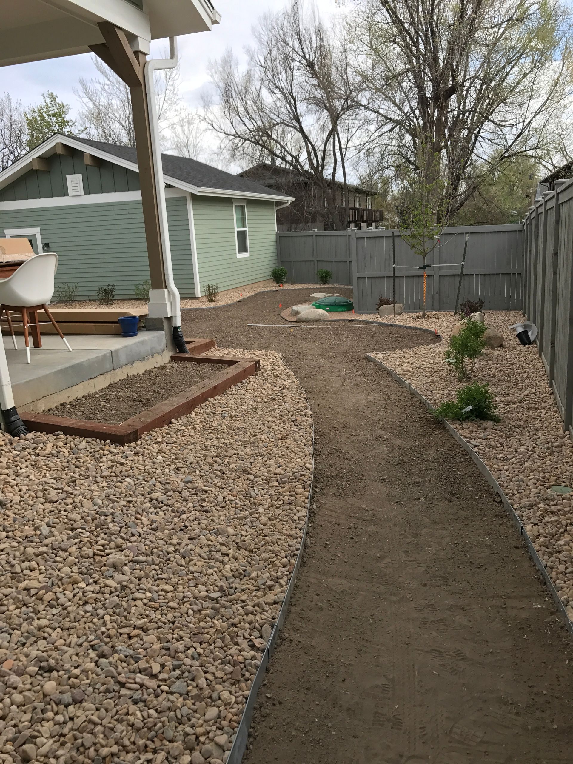 Backyard with gravel path leading to a green building and fence. Brown gravel surrounds the path.
