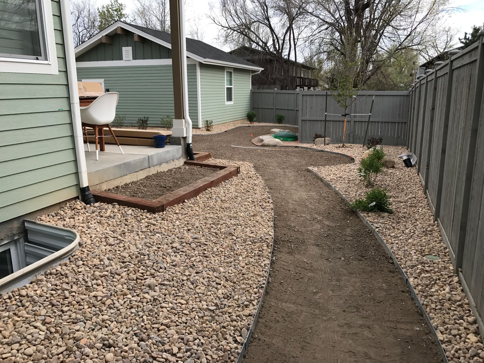 Backyard with gravel ground, dirt path, green shed, gray fence.