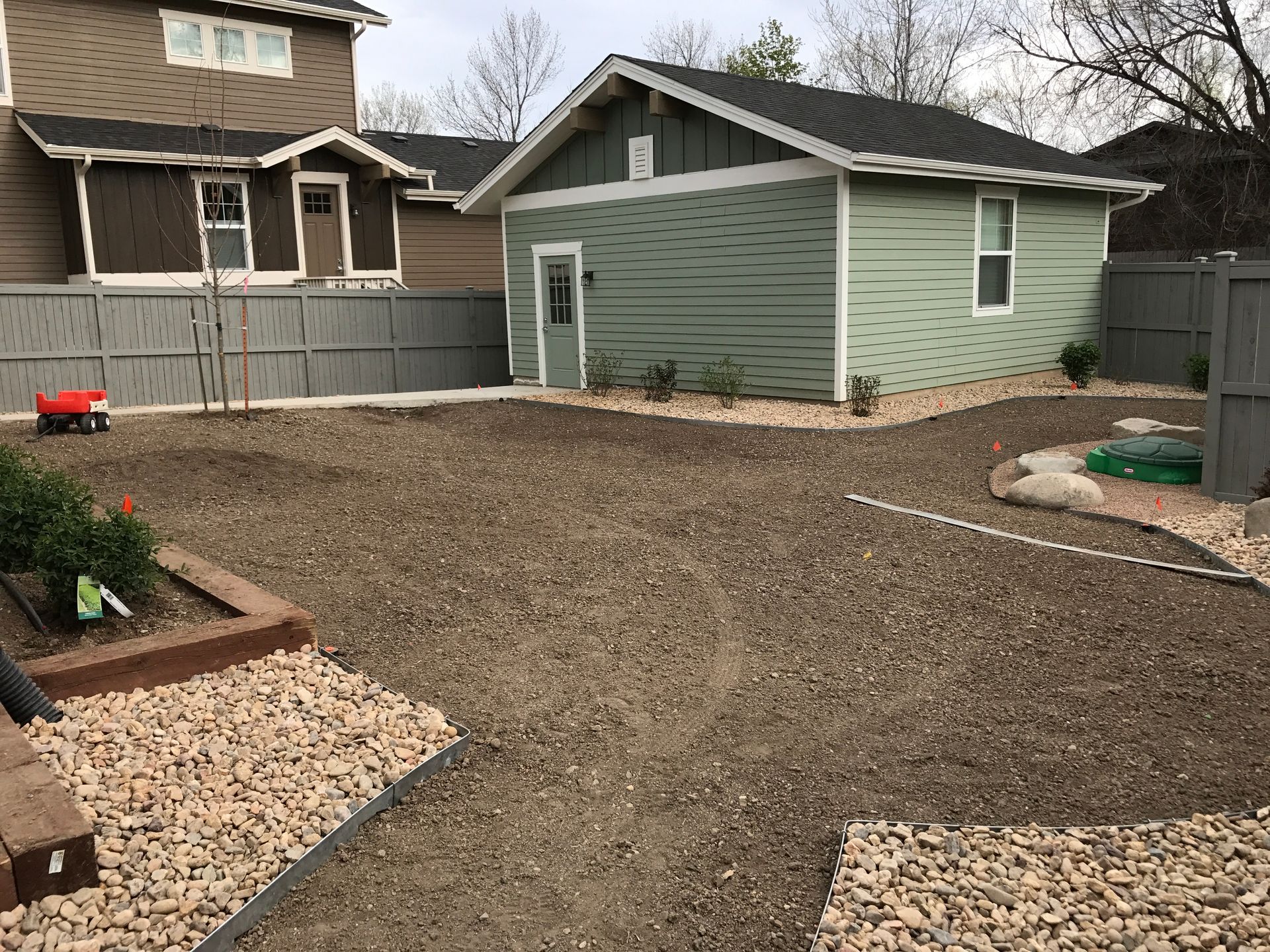 Backyard with brown gravel, a light green shed, and two houses.