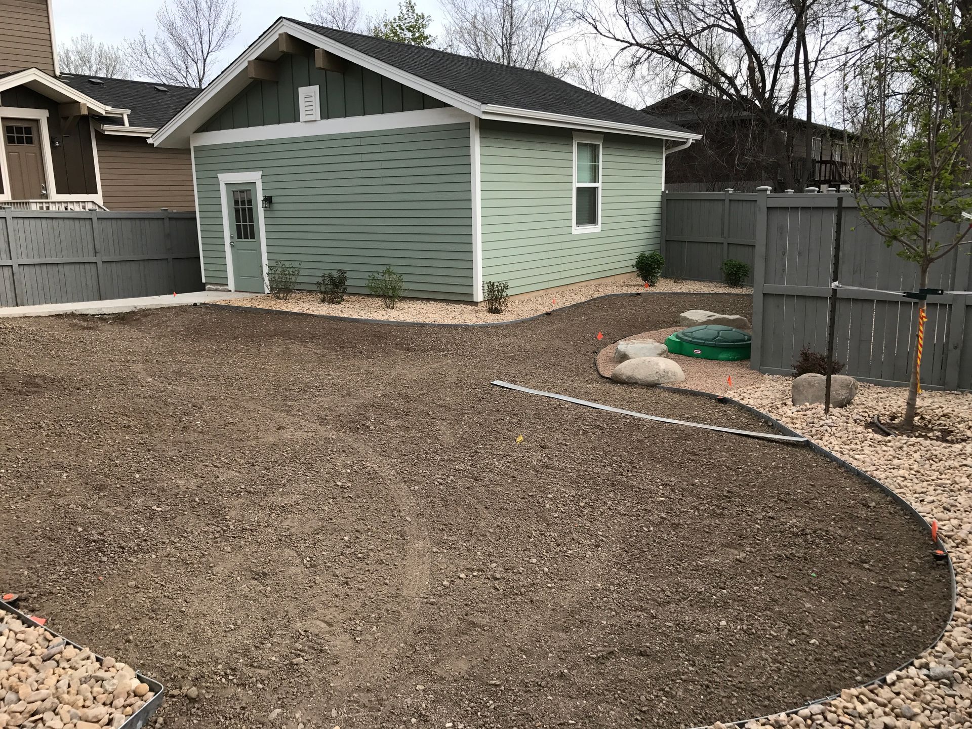 Backyard with gravel path leading to a green shed, gray fence, and a bare lawn.