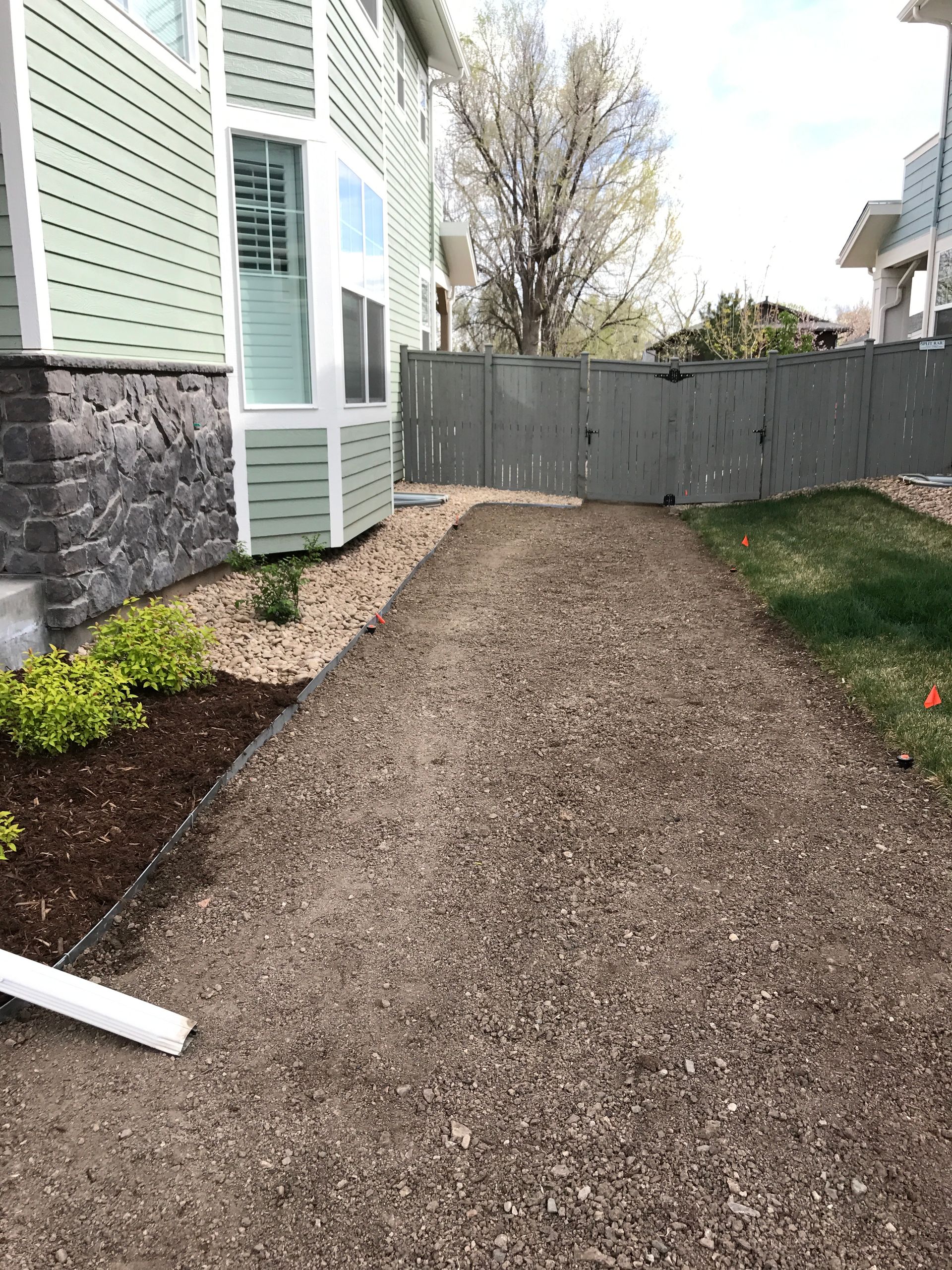 Gravel pathway beside a light green house with landscaping and a gray fence.