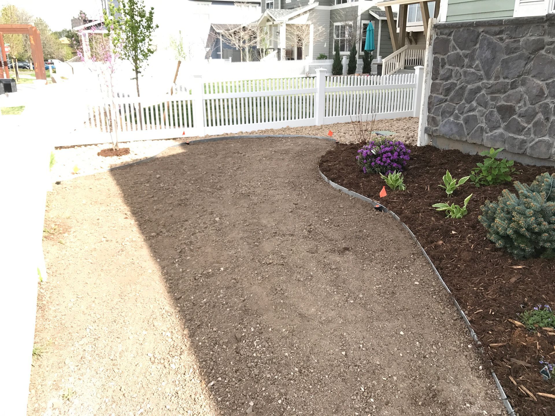 A gravel walkway leads to a house with a white picket fence and flower bed.