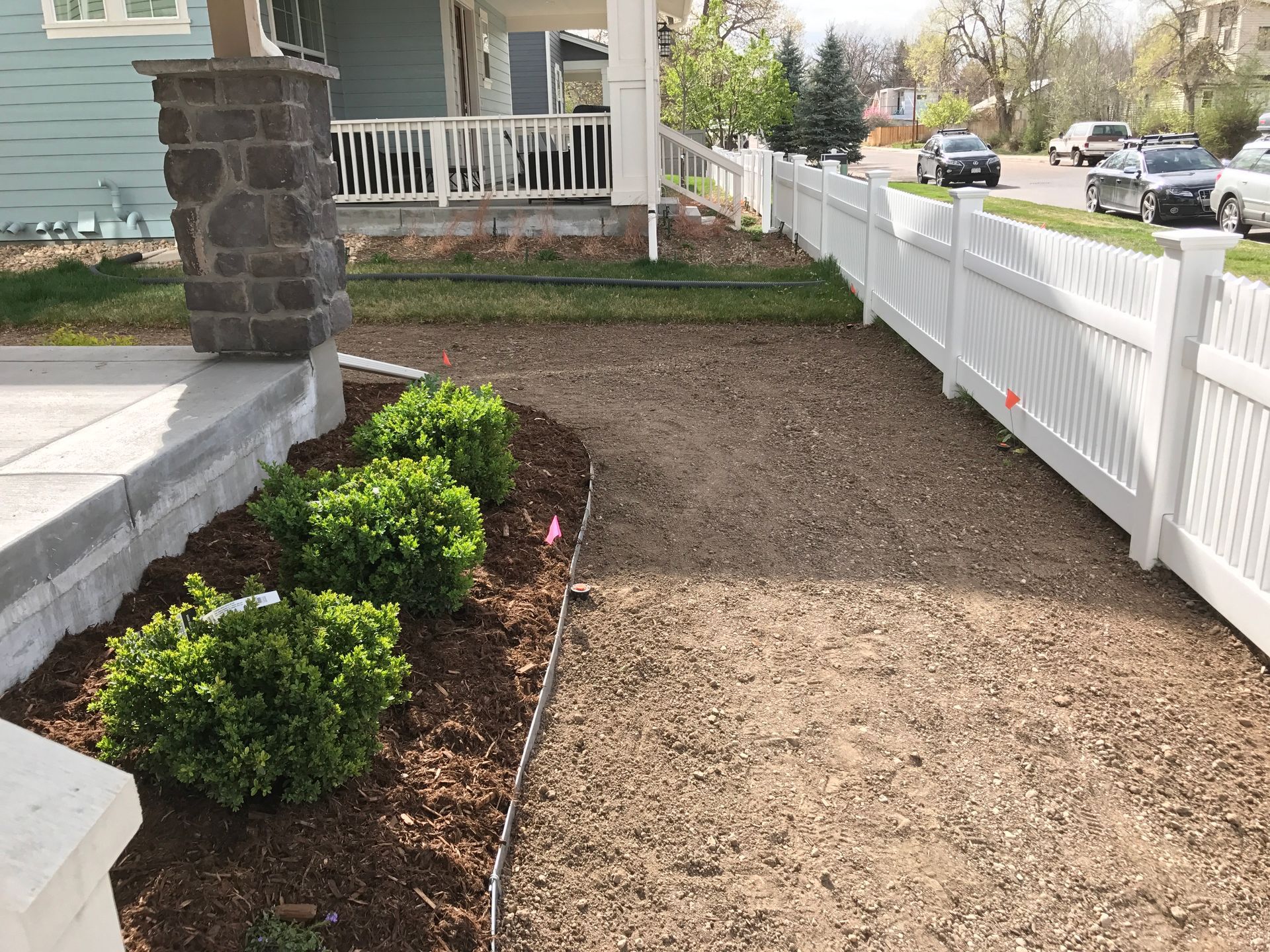 Front yard with white fence, gravel path, green bushes, and blue house.