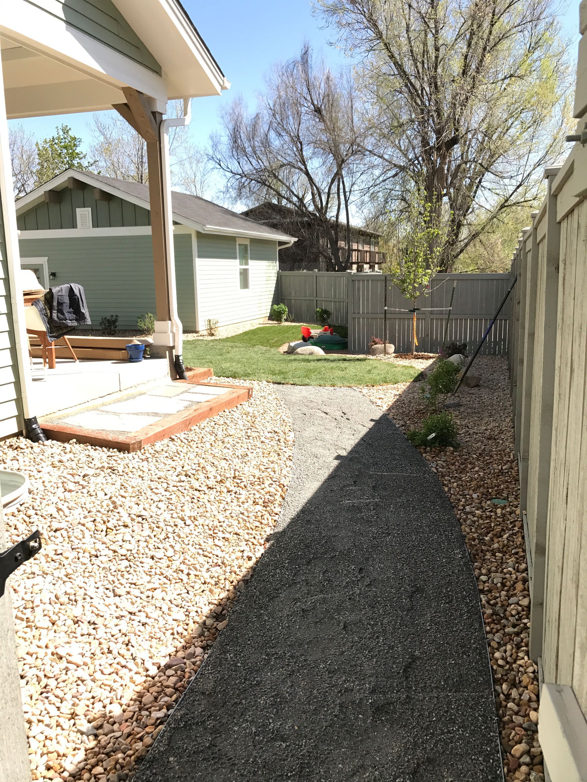 Gravel pathway beside a fence leads to a backyard with lawn, shed, and a wooden deck.