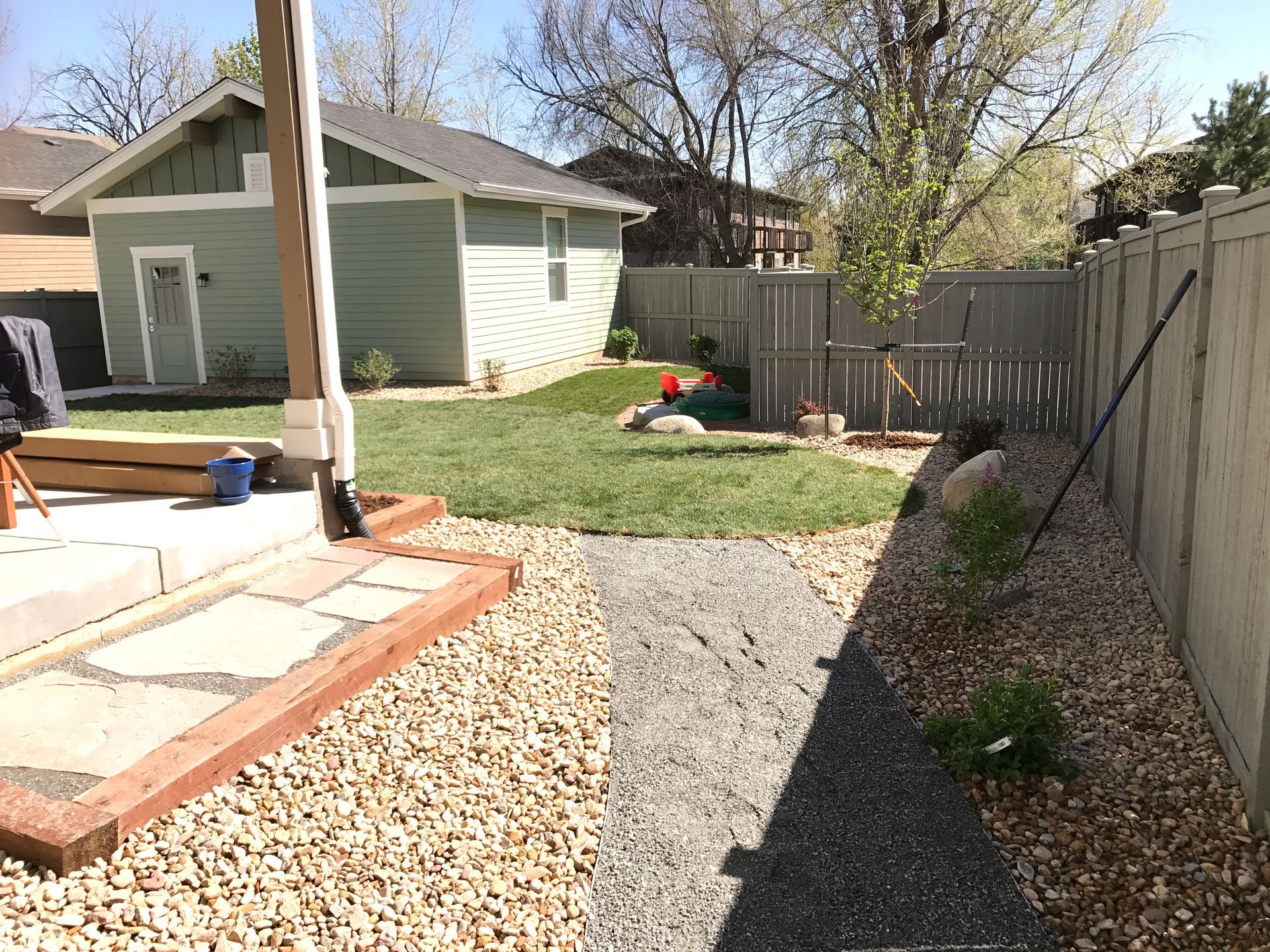 Backyard with flagstone patio, gravel path, green grass, light blue shed, and wood fence.