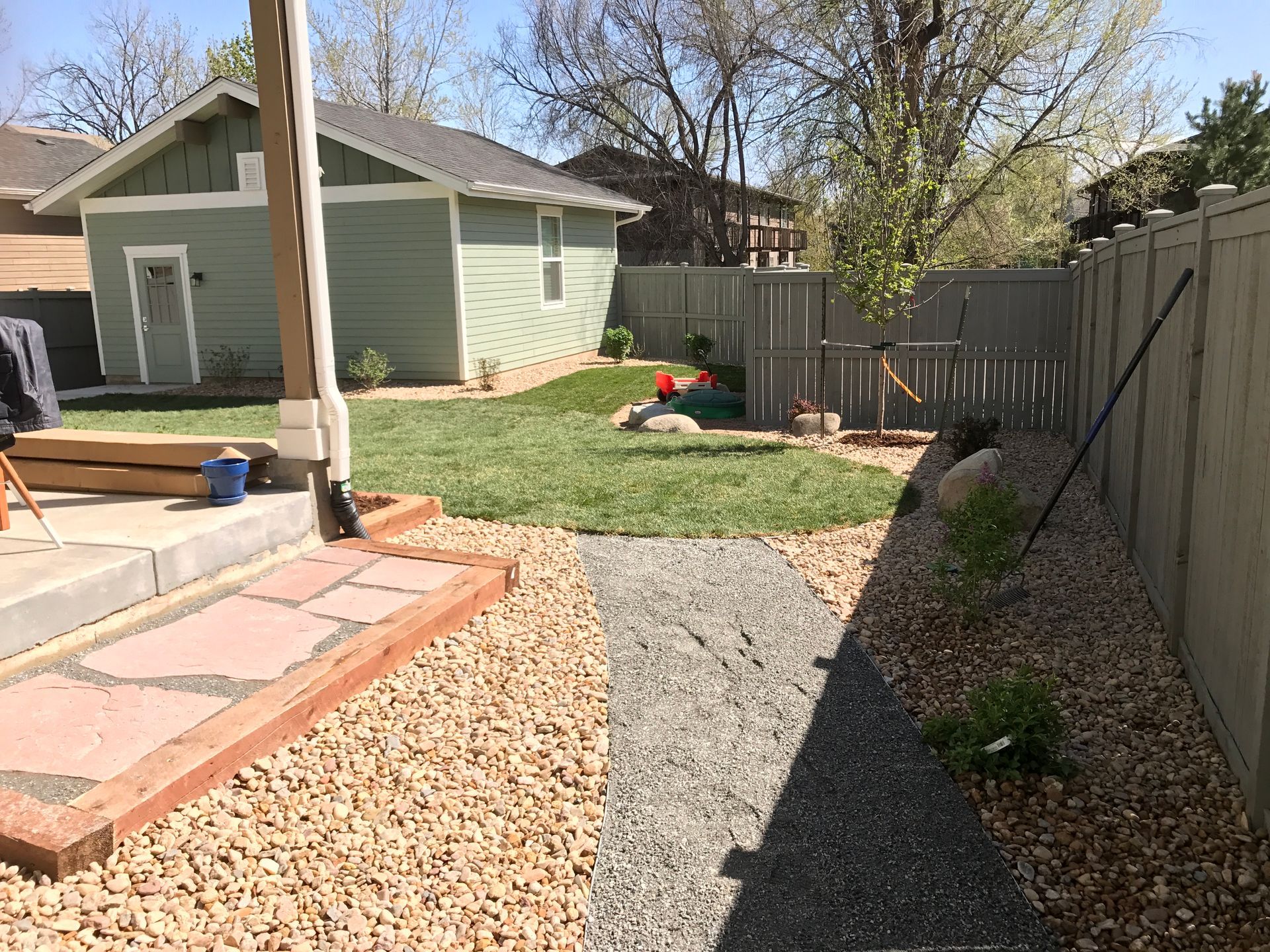 Backyard with gravel path, red brick patio, green lawn, shed, and gray fence.