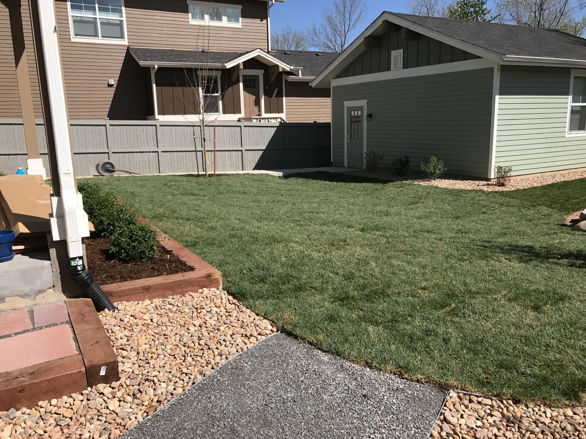 Backyard with freshly cut grass, gravel path, wooden planter box, and small shed.