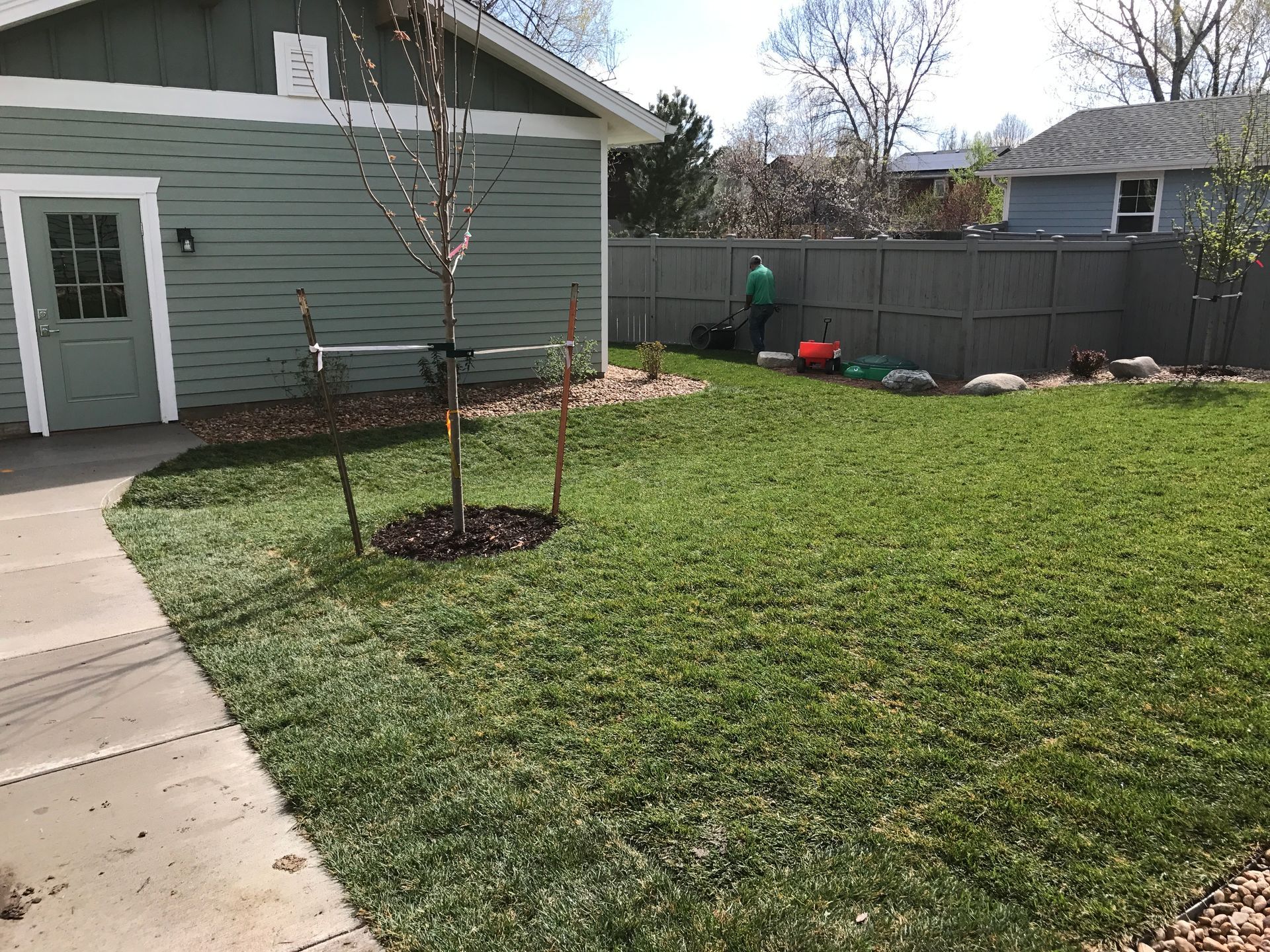 Green lawn with a garage, sidewalk, and person mowing.