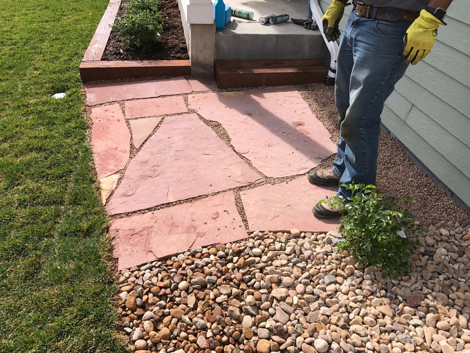 Person installing red stone walkway next to a house with gravel and grass.