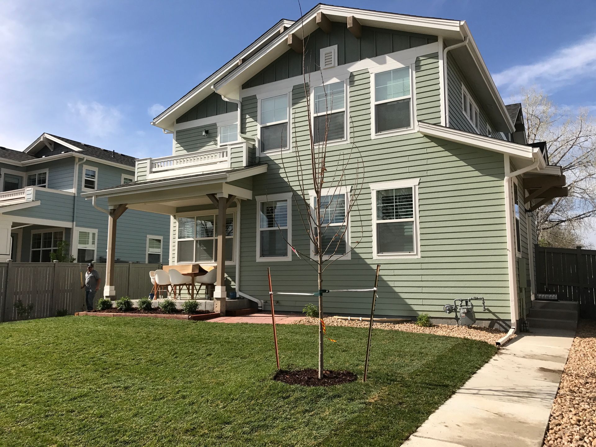 Two-story green house with white trim, porch, and a small tree in the front yard.