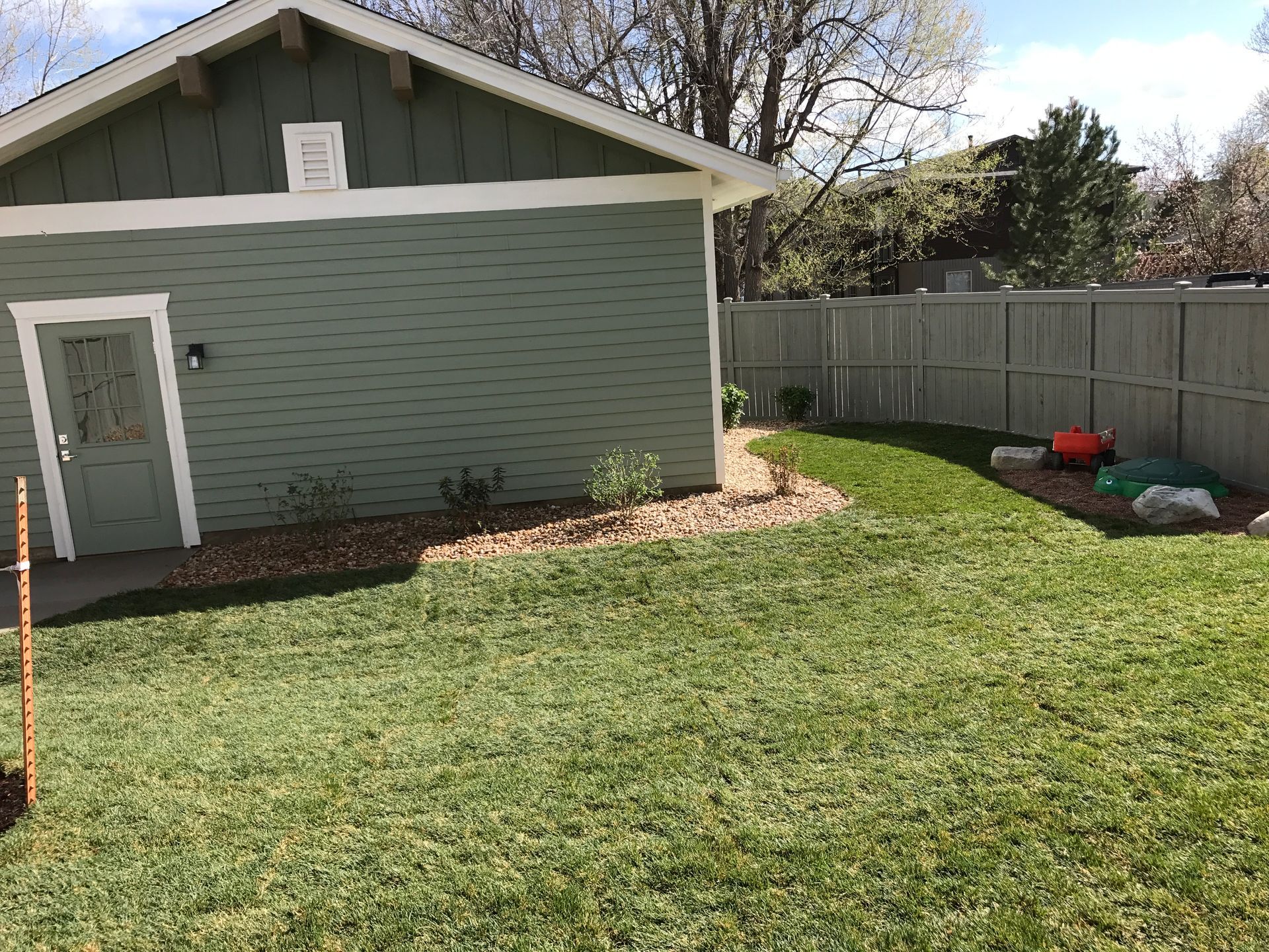 Green-sided building with a light green door and a fenced-in grassy yard.