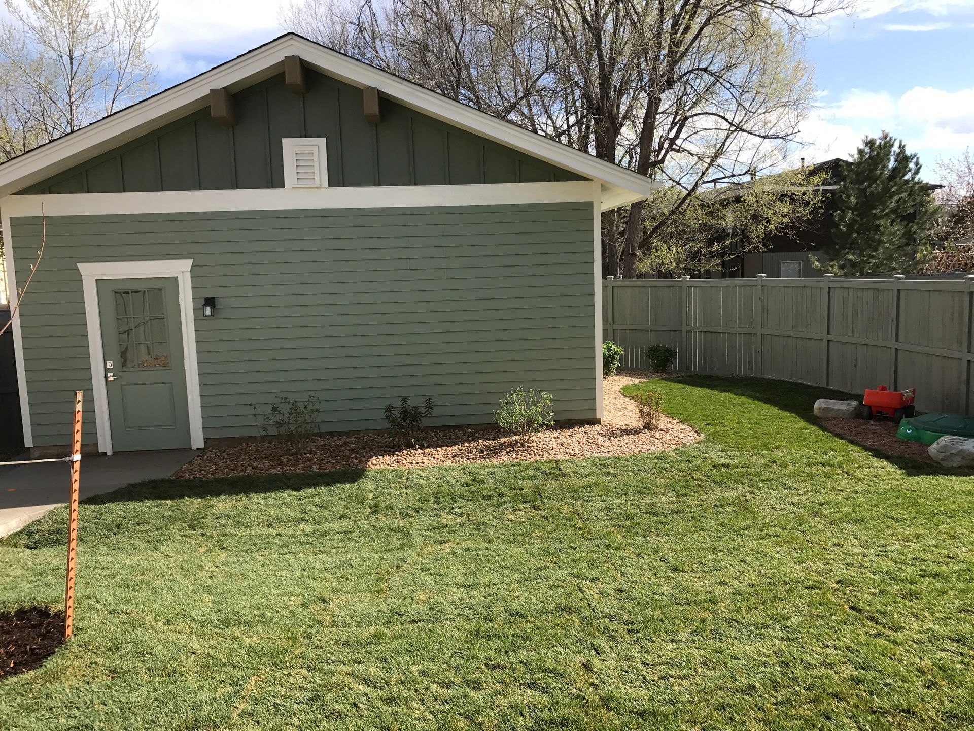 Green building with a door, next to a grassy yard and wooden fence.