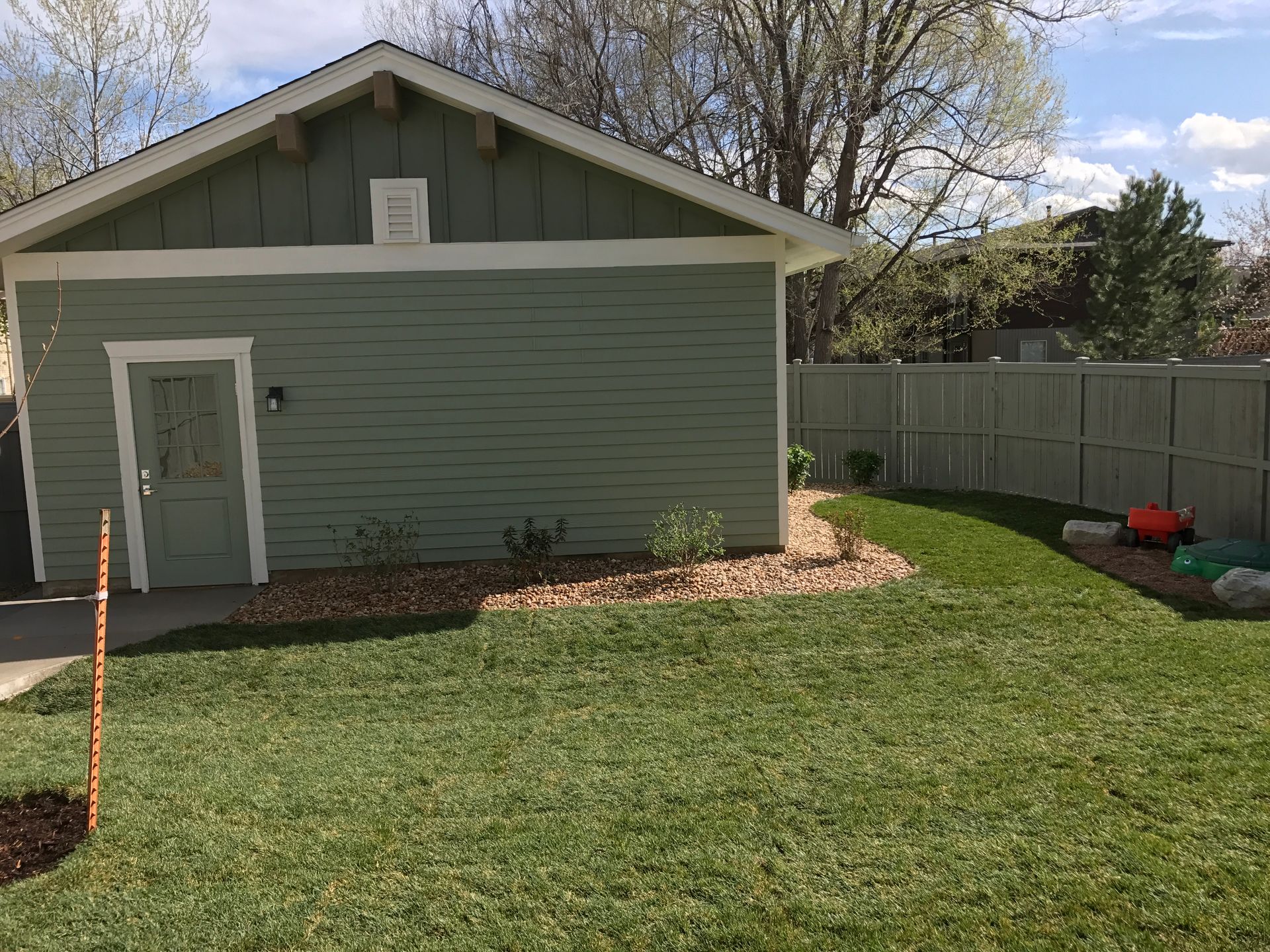 Green-painted garage with matching door in a backyard with green grass and a wooden fence.
