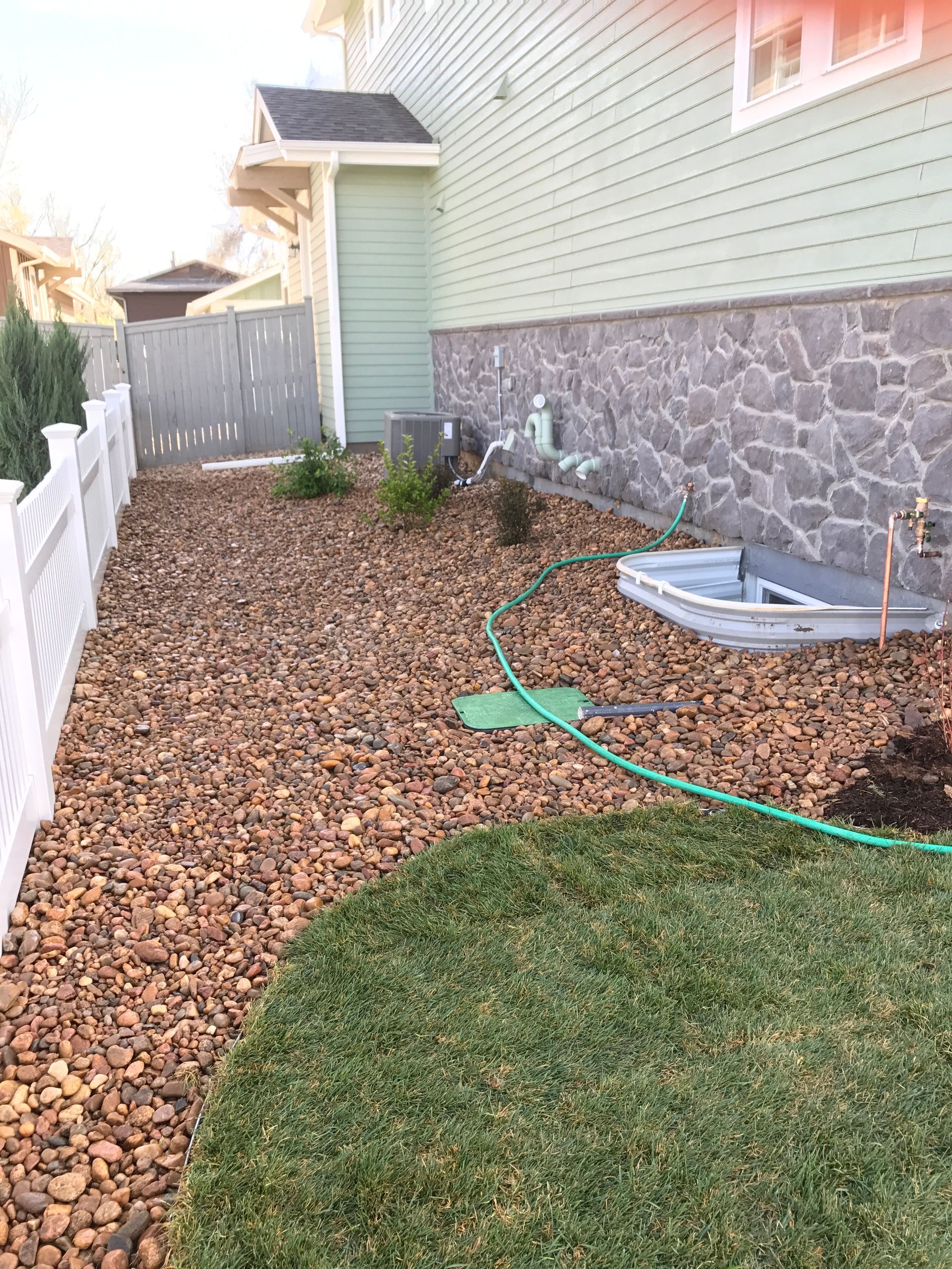 Side yard with gravel, grass, and a white fence next to a house with stone siding.