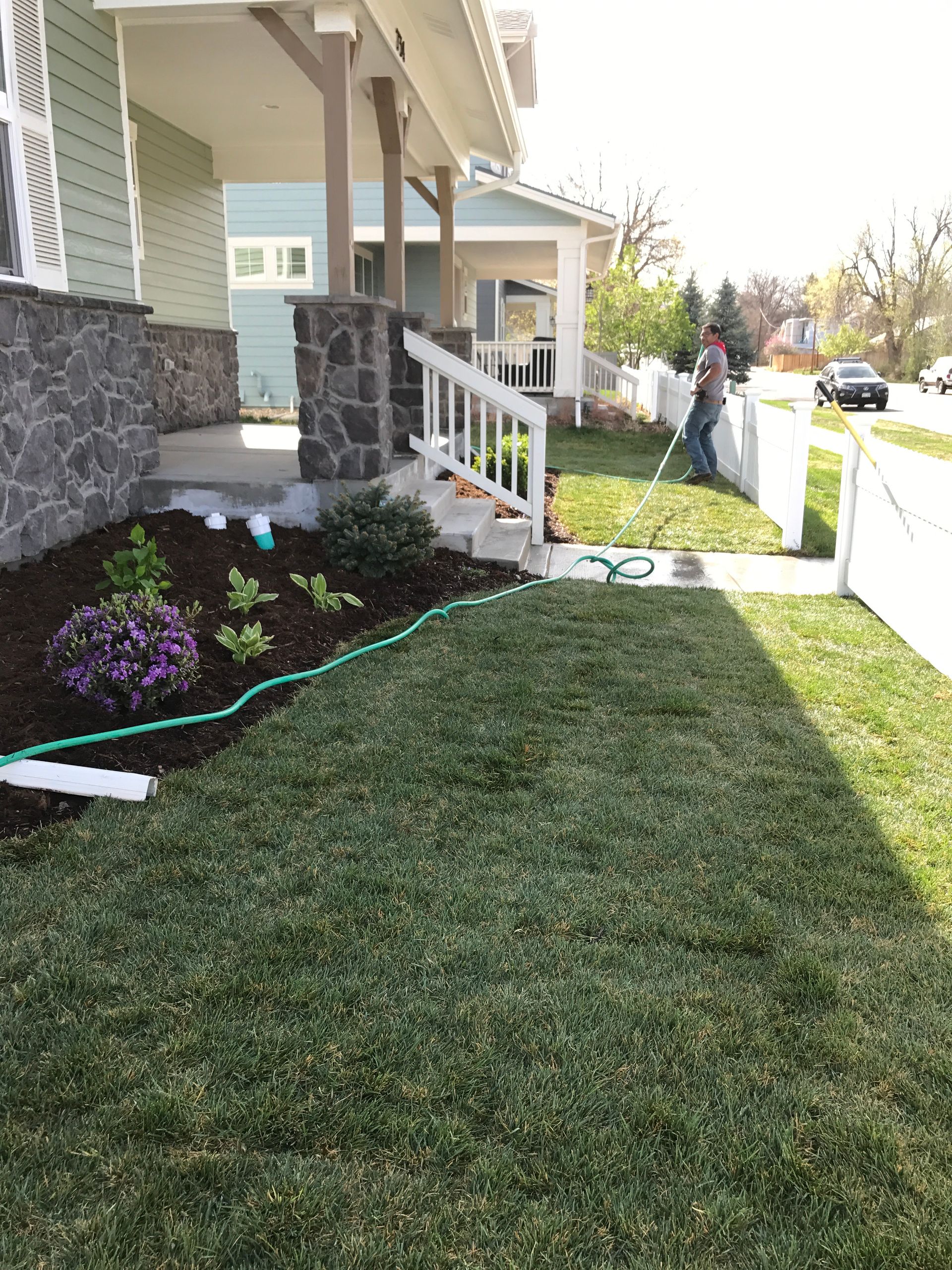 Person waters a newly landscaped yard with a green hose, in front of a house.