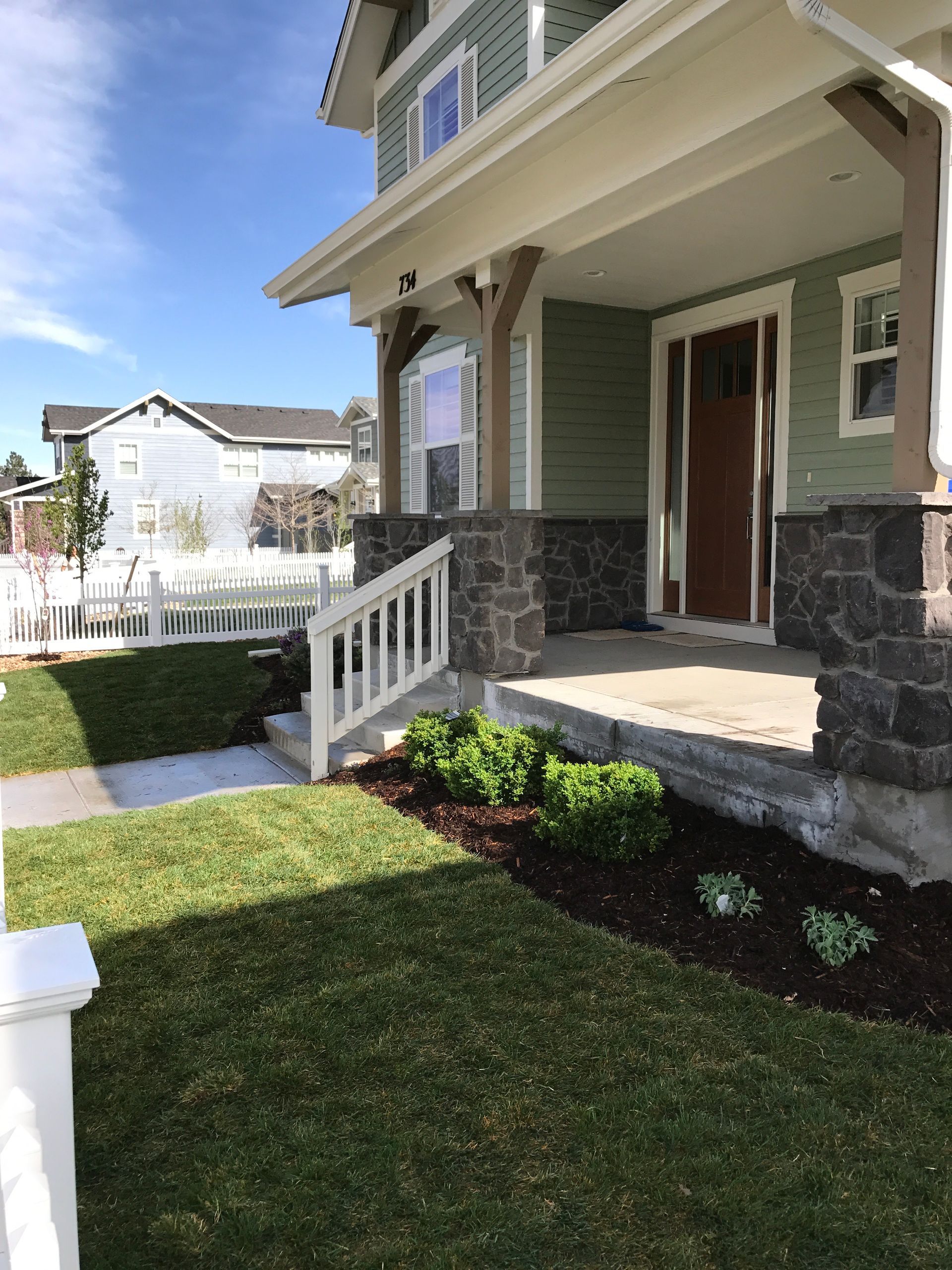 Green house with stone accents, white railing, and manicured landscaping.