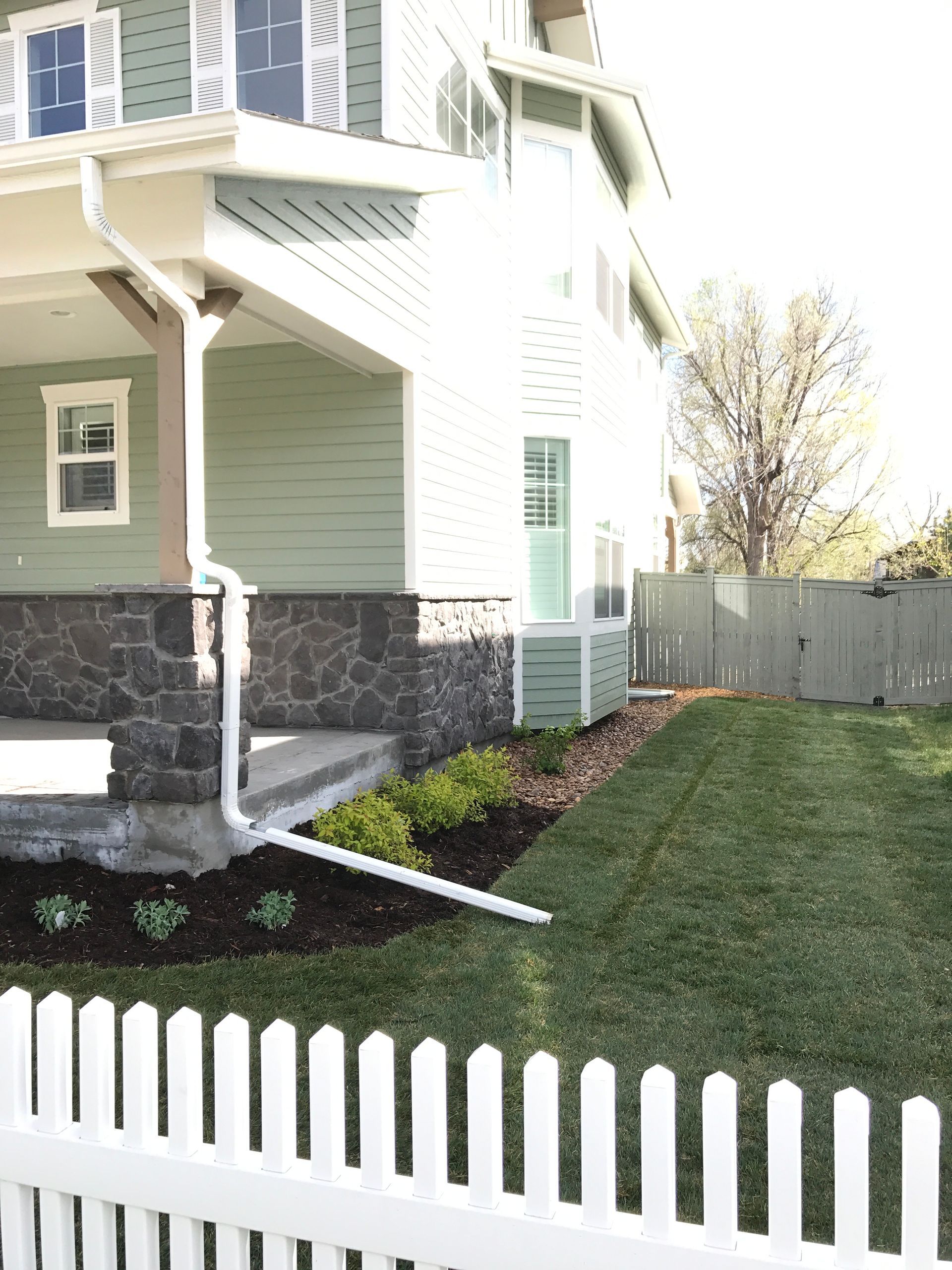A green house with a white picket fence, a small garden, and newly laid grass.
