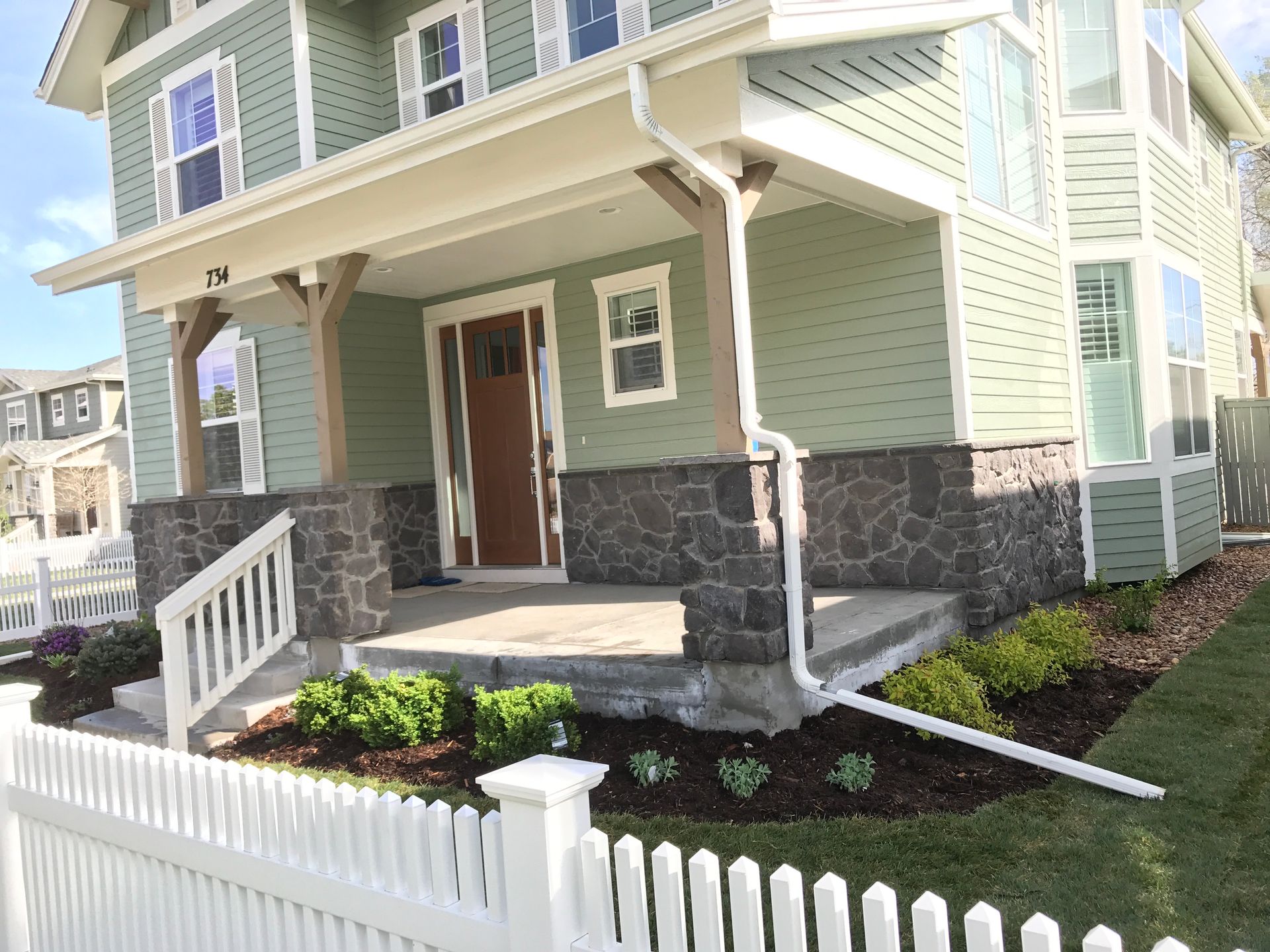 Green house with stone accents, porch, white picket fence, and landscaped yard.
