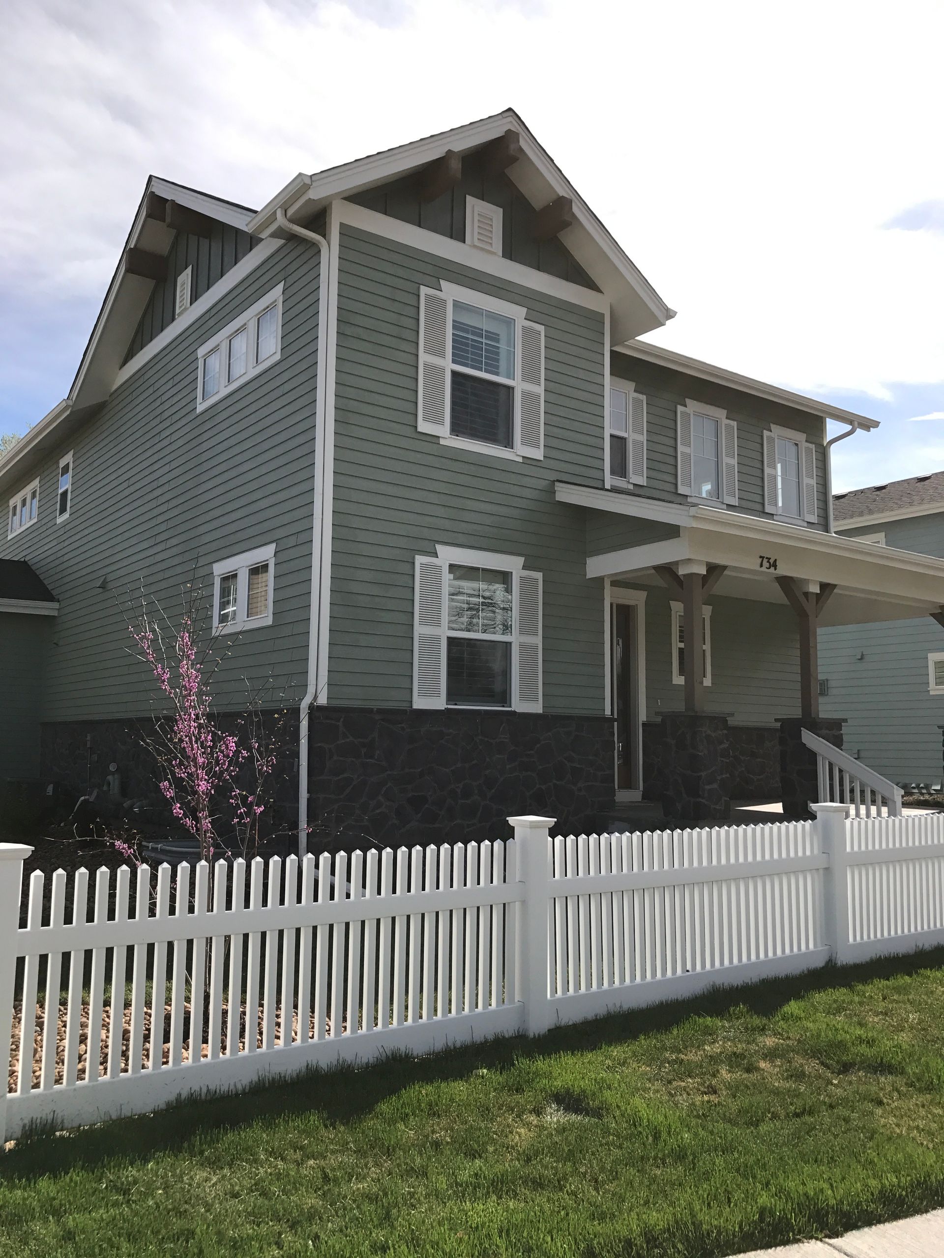 Two-story green house with white picket fence, white shutters, and porch.