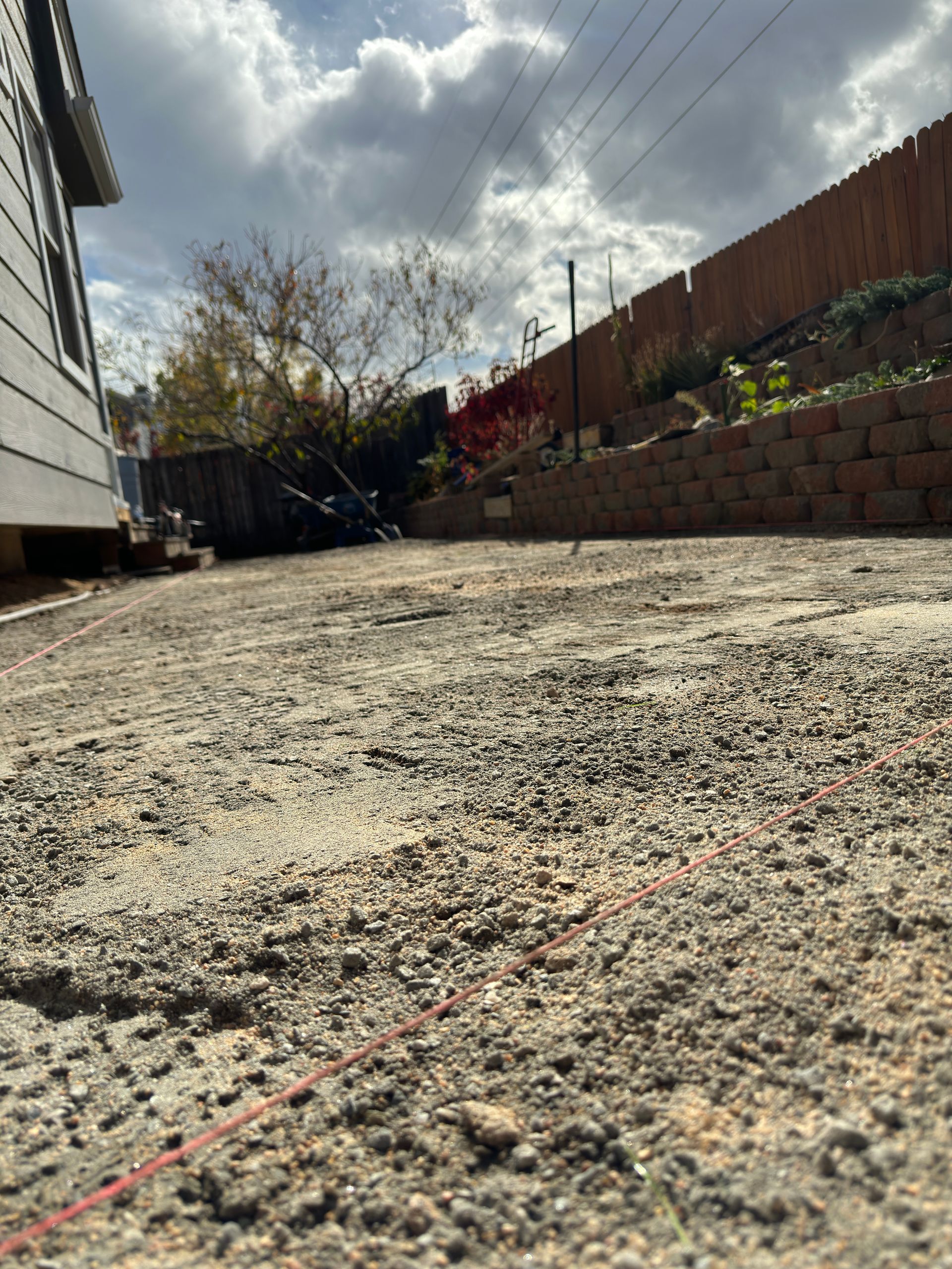 Gravel yard, string line, house, retaining wall, cloudy sky.