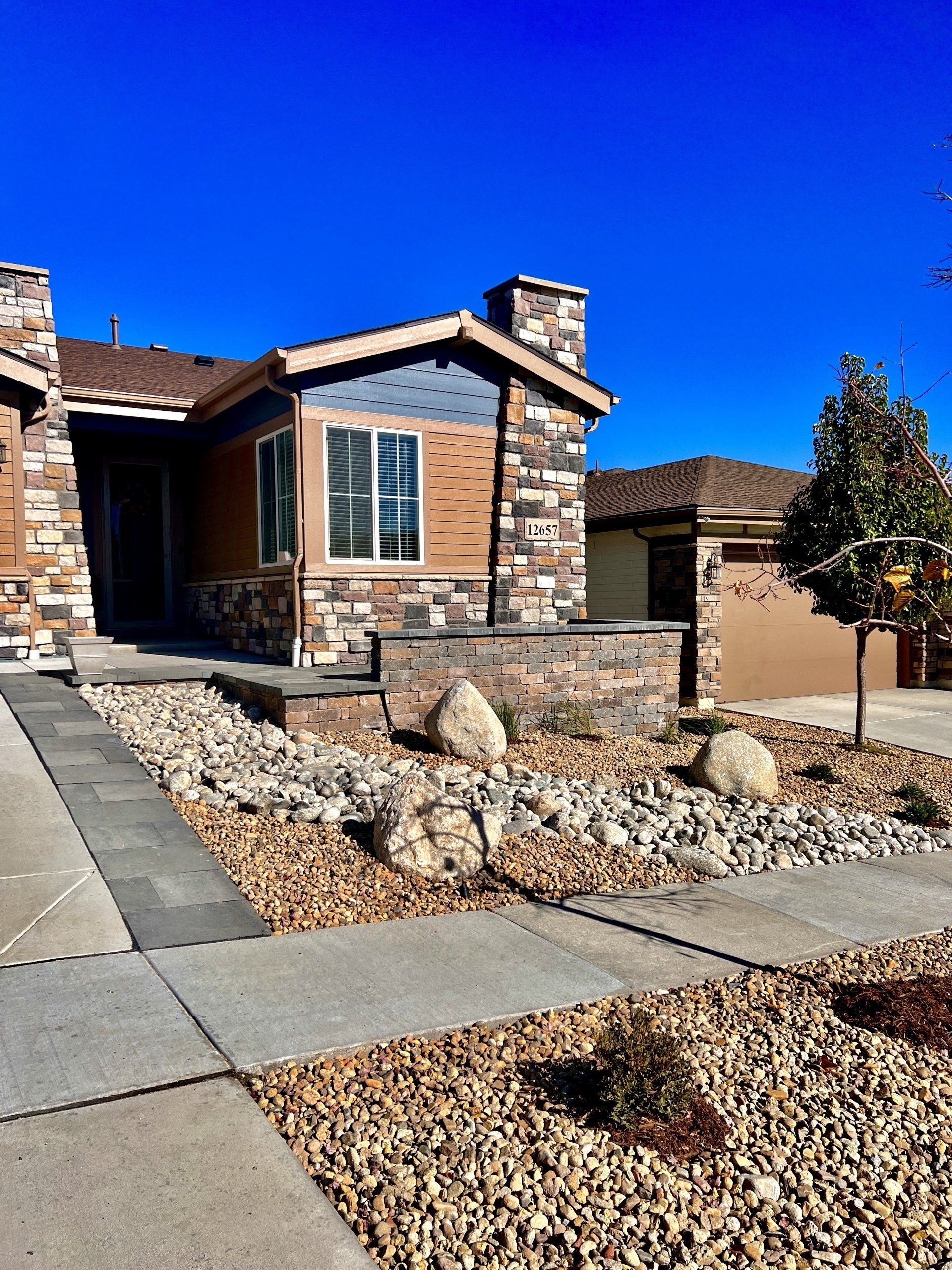 House front with rock landscaping, blue sky. Brown and stone exterior.