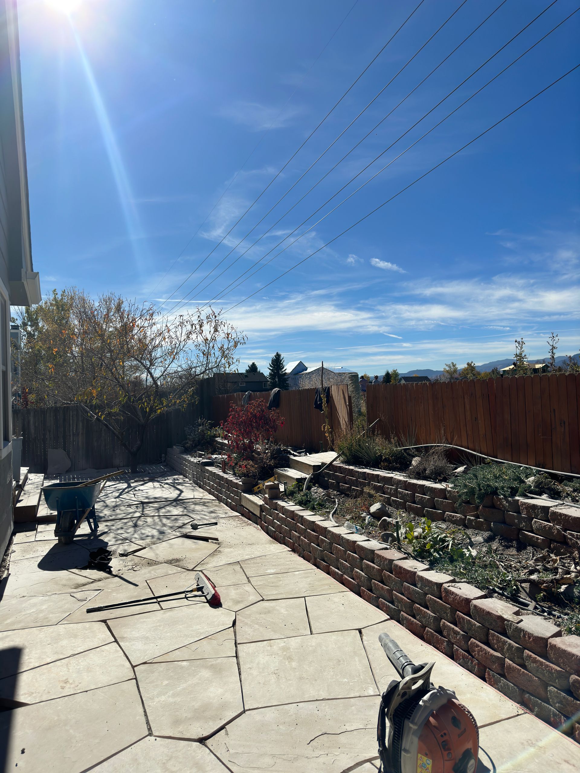 Backyard patio with brick planters, sunny blue sky, and power saw.