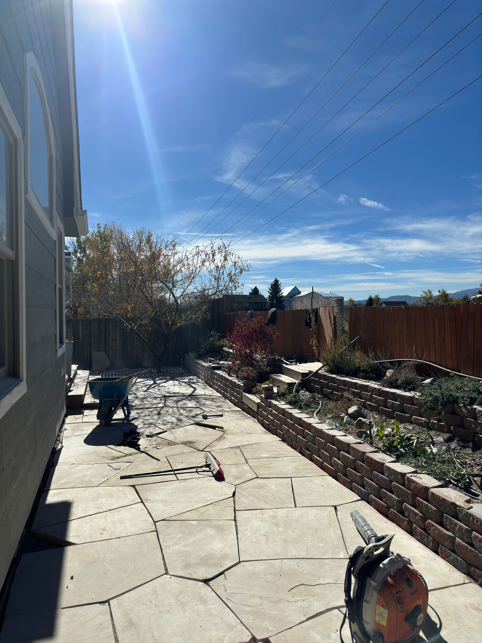 Backyard patio with brick planters, sunny blue sky, and tools.