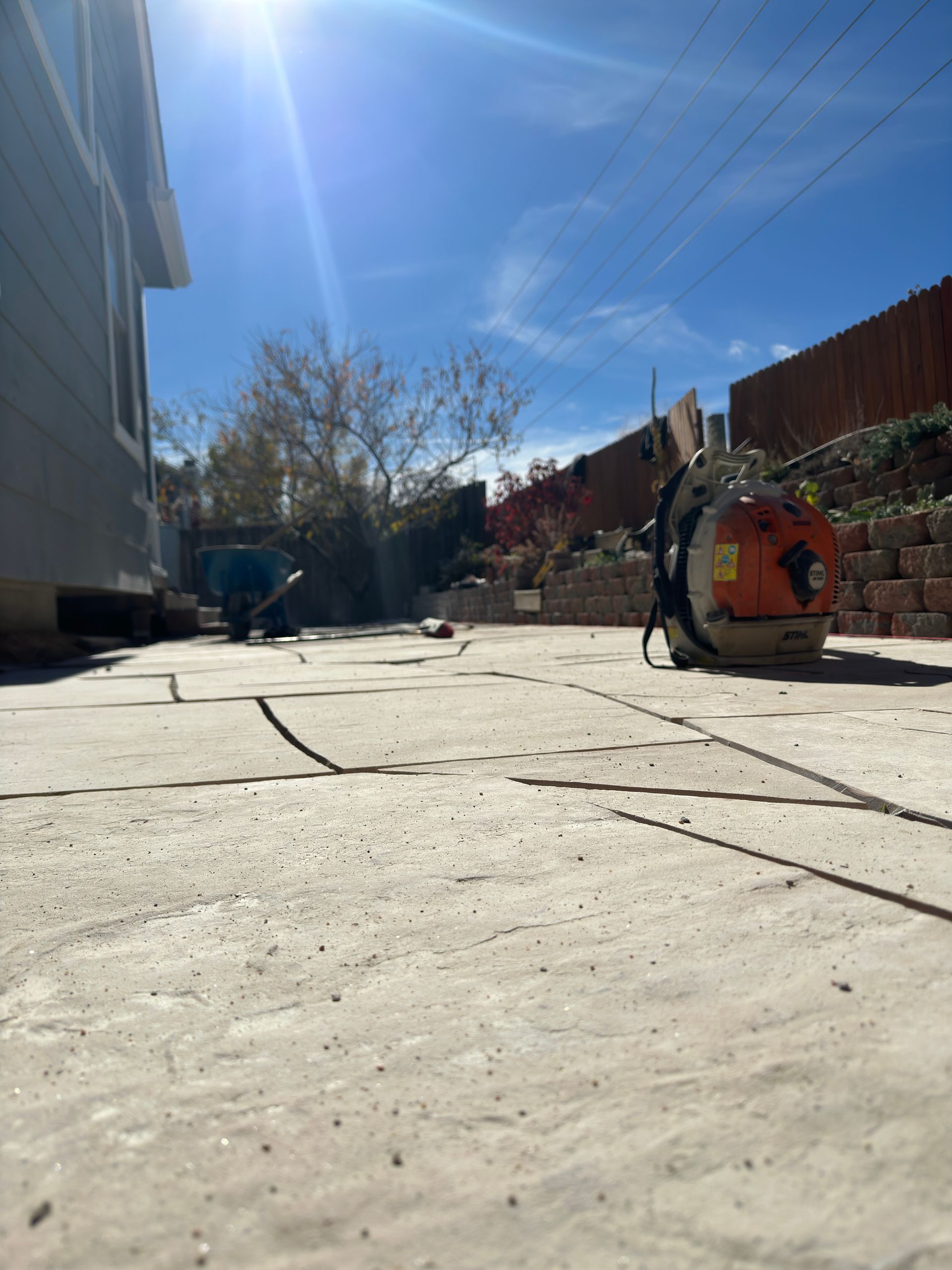 Patio with a leaf blower, blue sky, and a house.