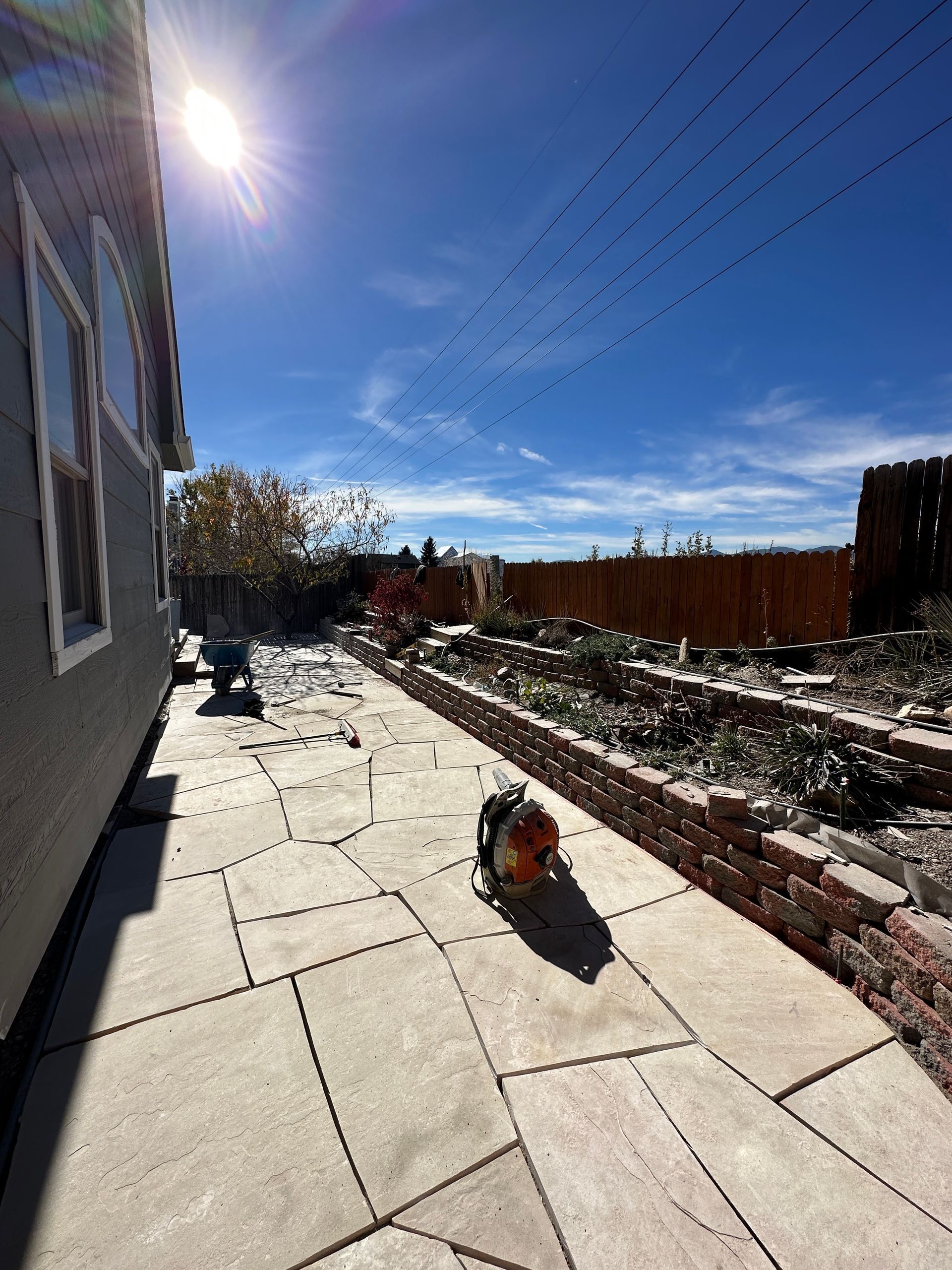 Sunny backyard with a concrete patio, brick garden bed, and a circular saw in the center.