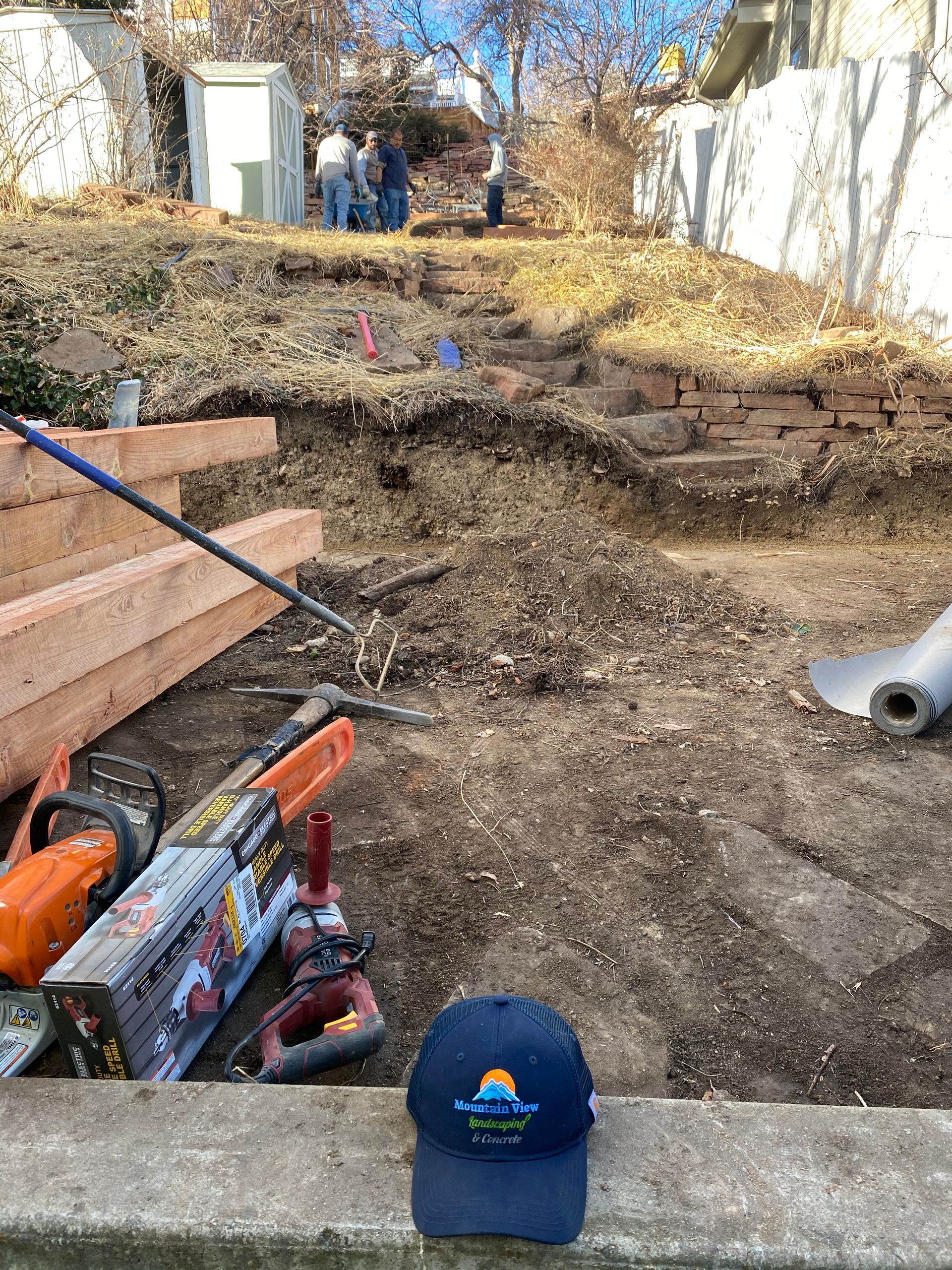 Construction site with tools, a retaining wall, and people in the background. A blue hat is in the foreground.