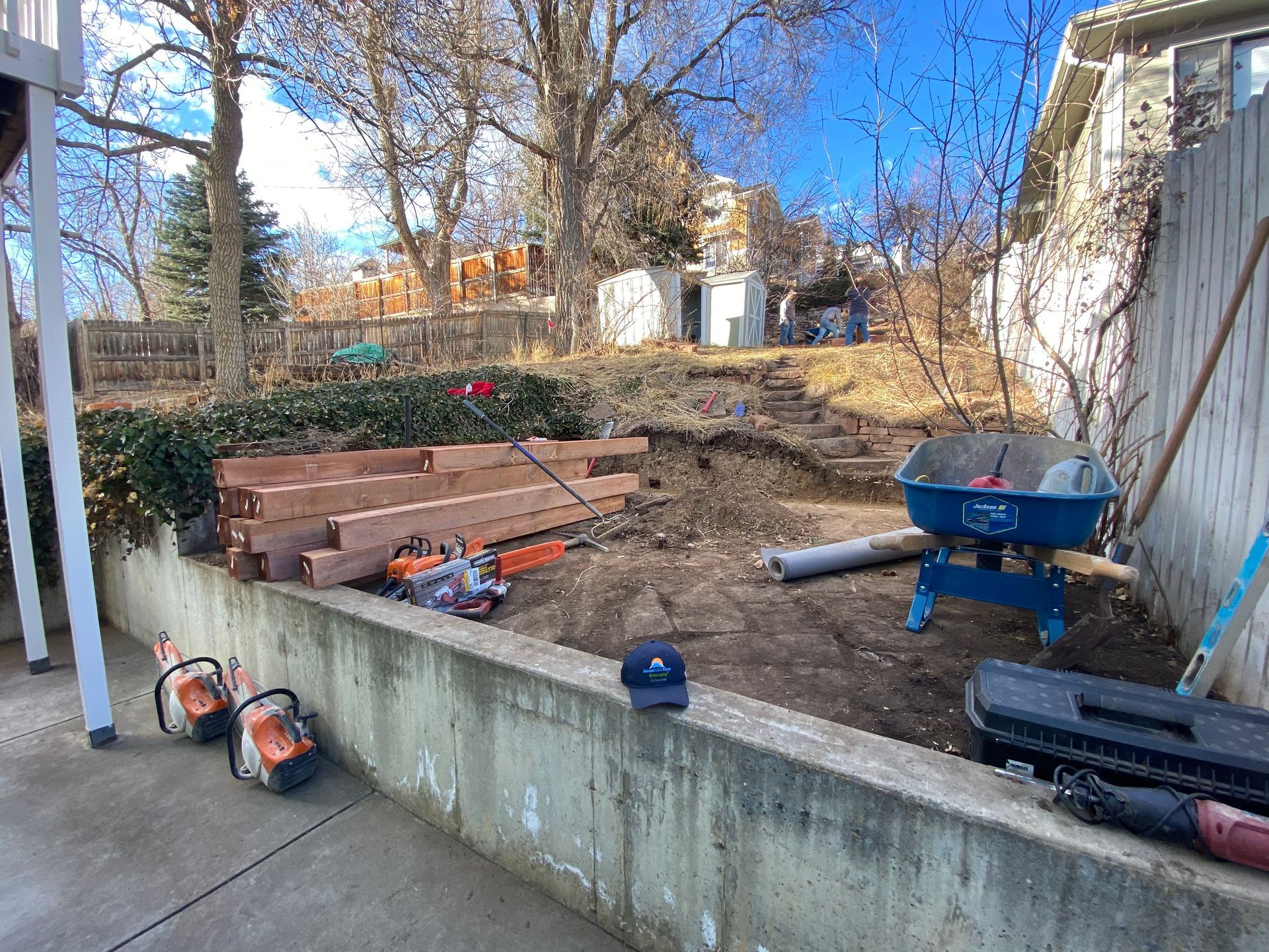 Construction site. Lumber and tools on a concrete wall; wheelbarrow and shed in the background.