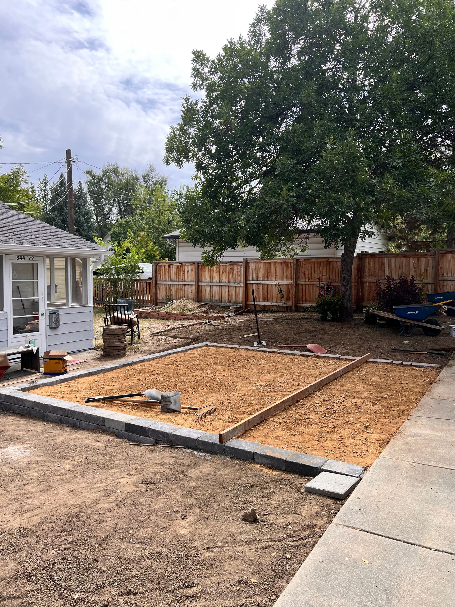 Backyard with a raised garden bed, brown mulch, grey border, and a mature tree.
