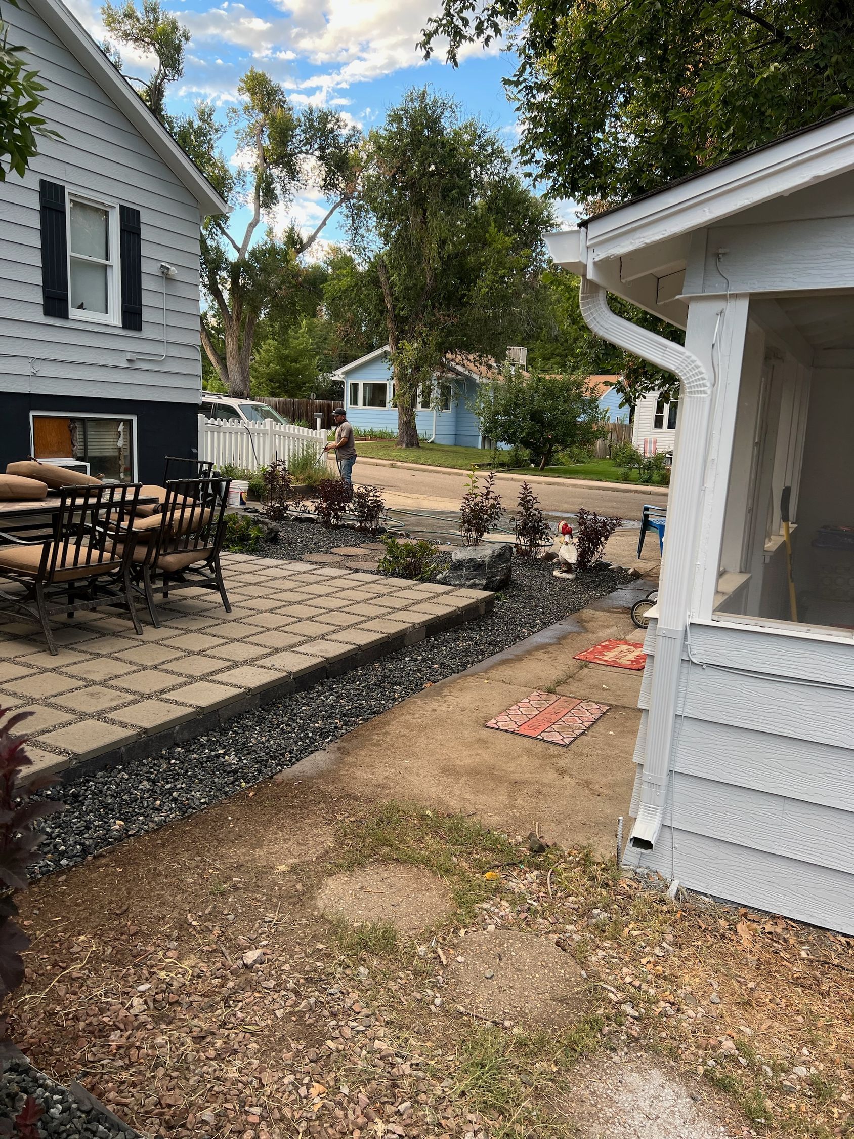 Backyard patio with gravel border, chairs, and nearby houses under a blue sky.