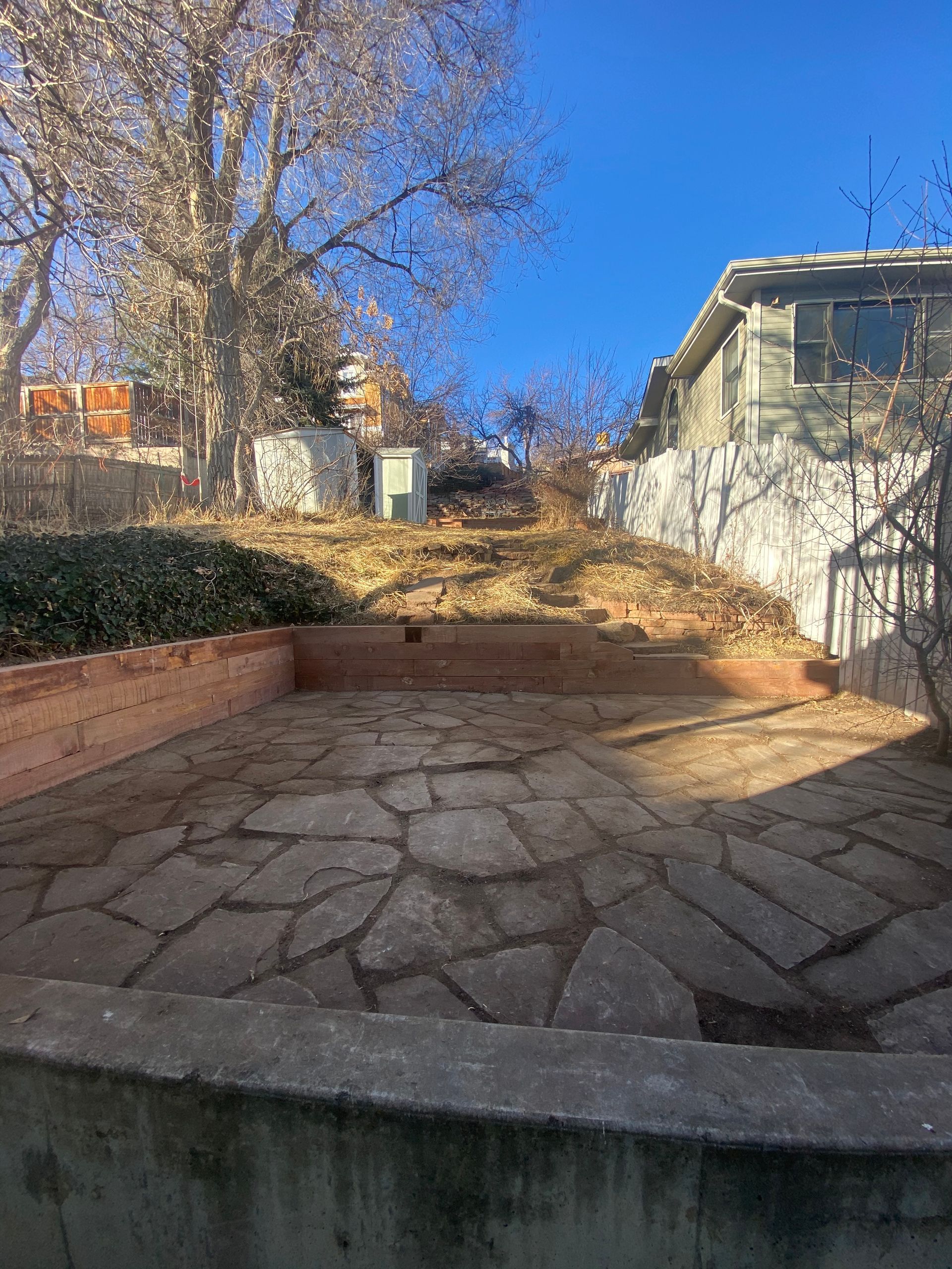 Stone patio with raised beds in foreground, hillside in background with a house.