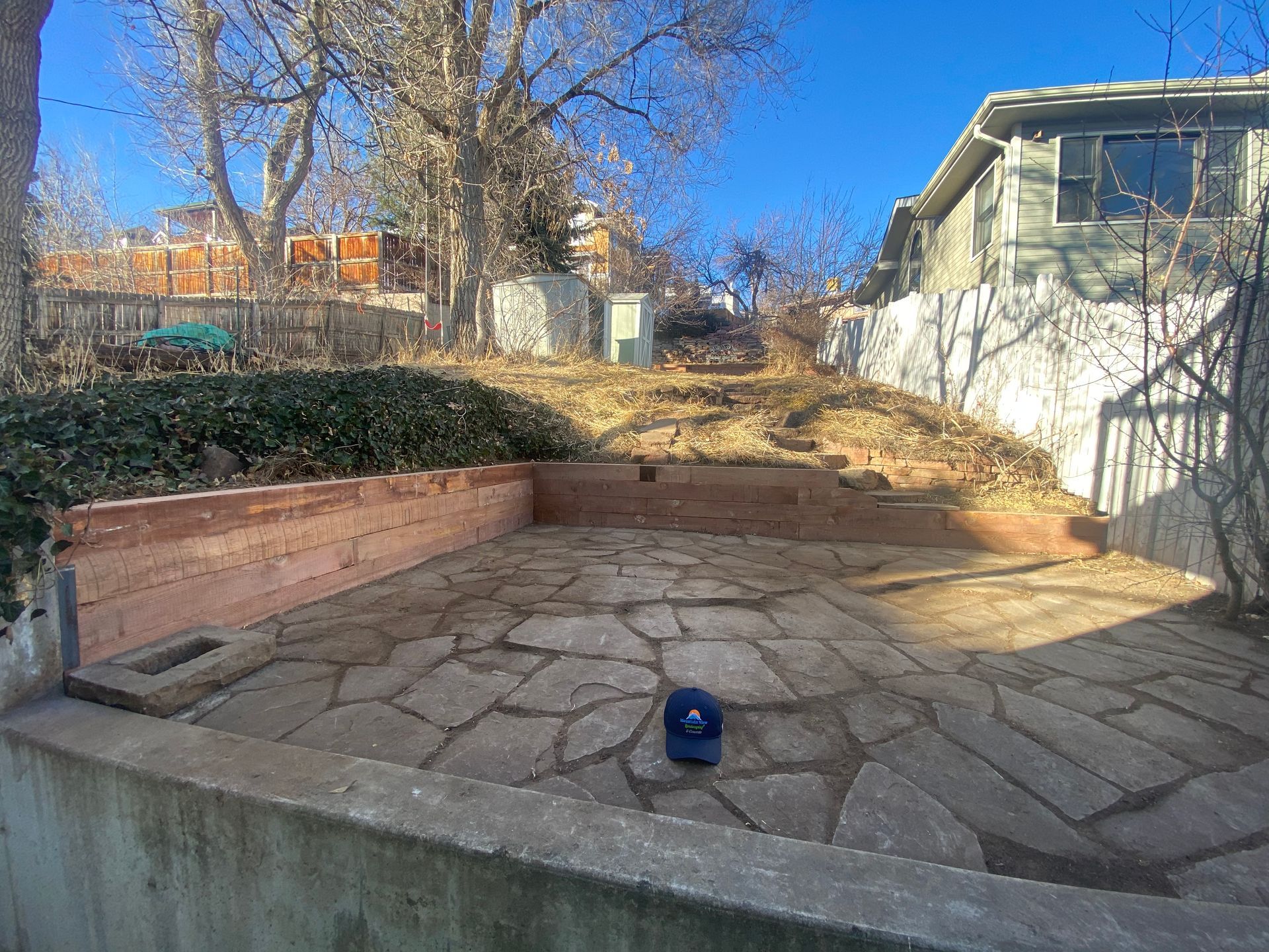 Backyard with stone patio, retaining walls, sloped hill, blue cap.