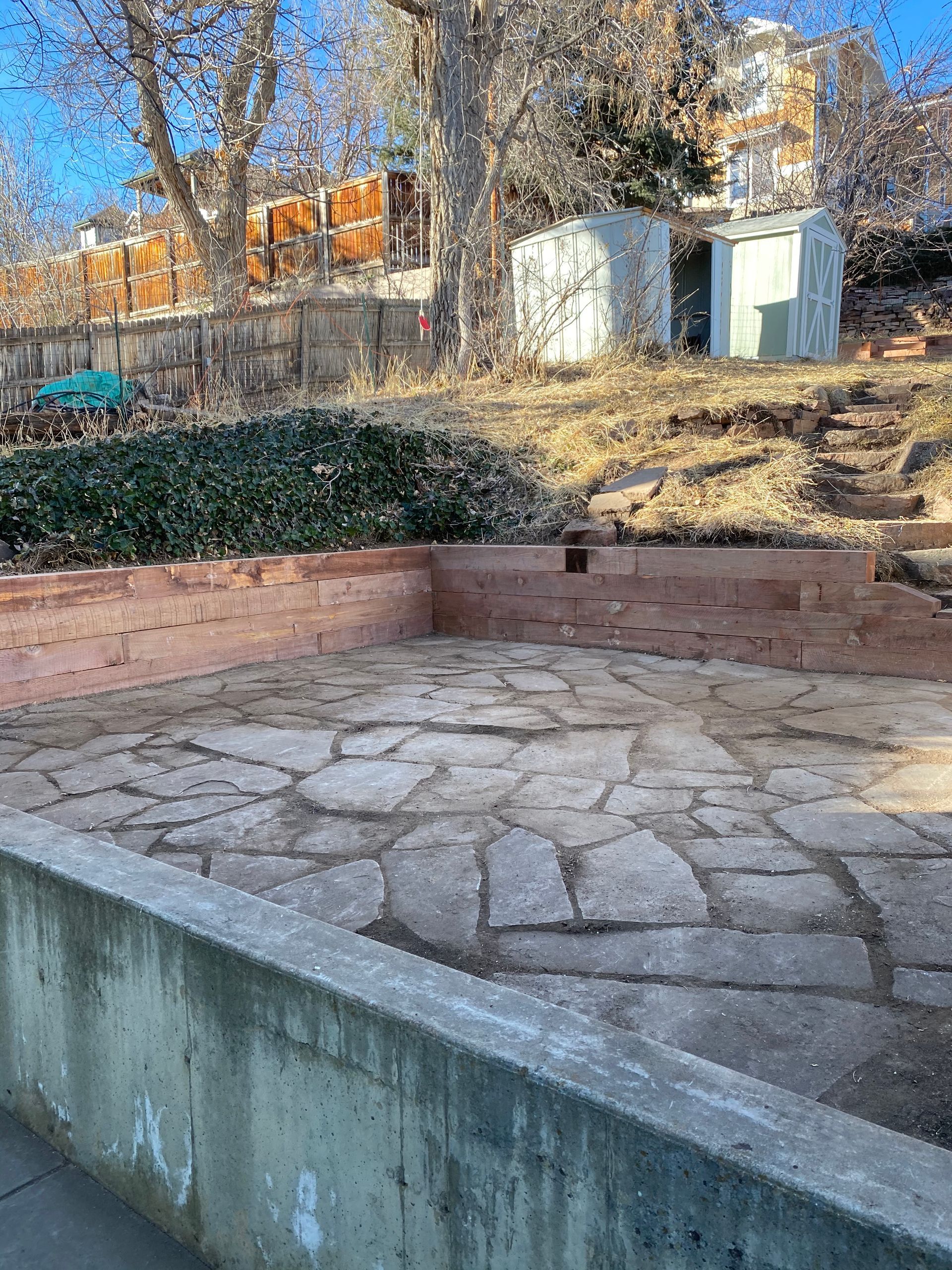 Stone patio and retaining wall in a backyard setting.