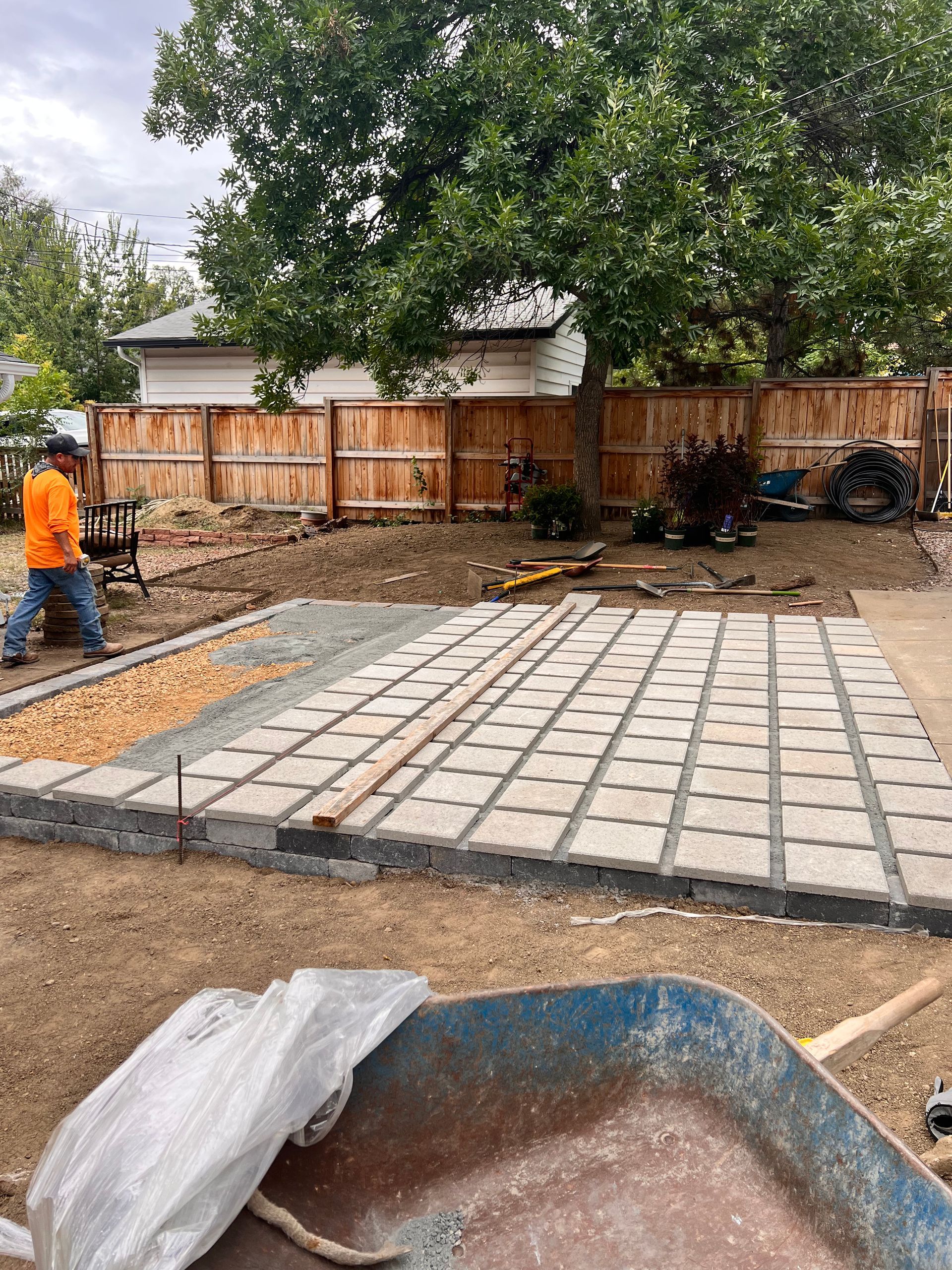 Construction worker building a patio with pavers and gravel, in a backyard setting.