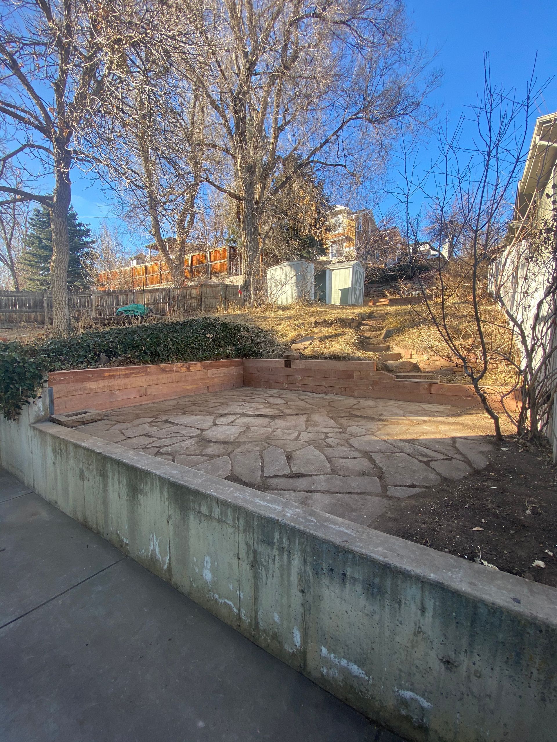 Concrete patio with a retaining wall, trees, and buildings on a sunny day.