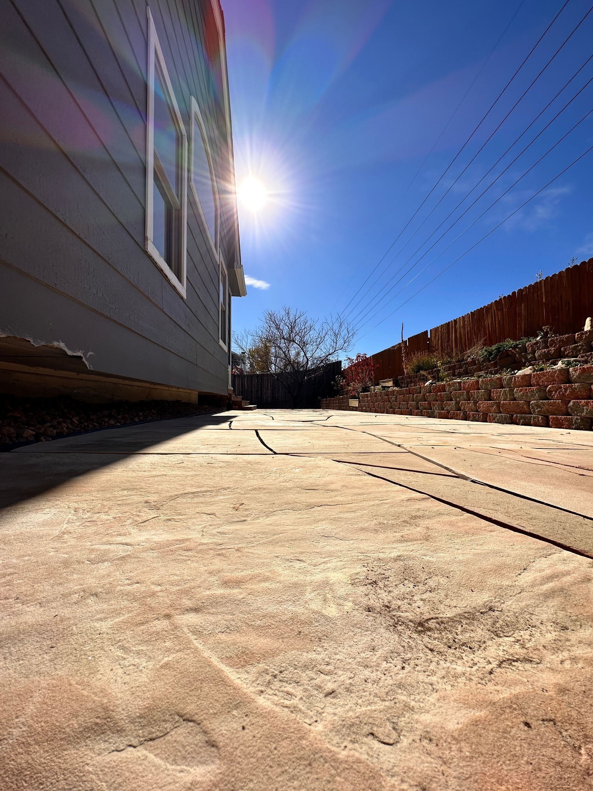 Sun shining over a concrete patio next to a house with blue siding.