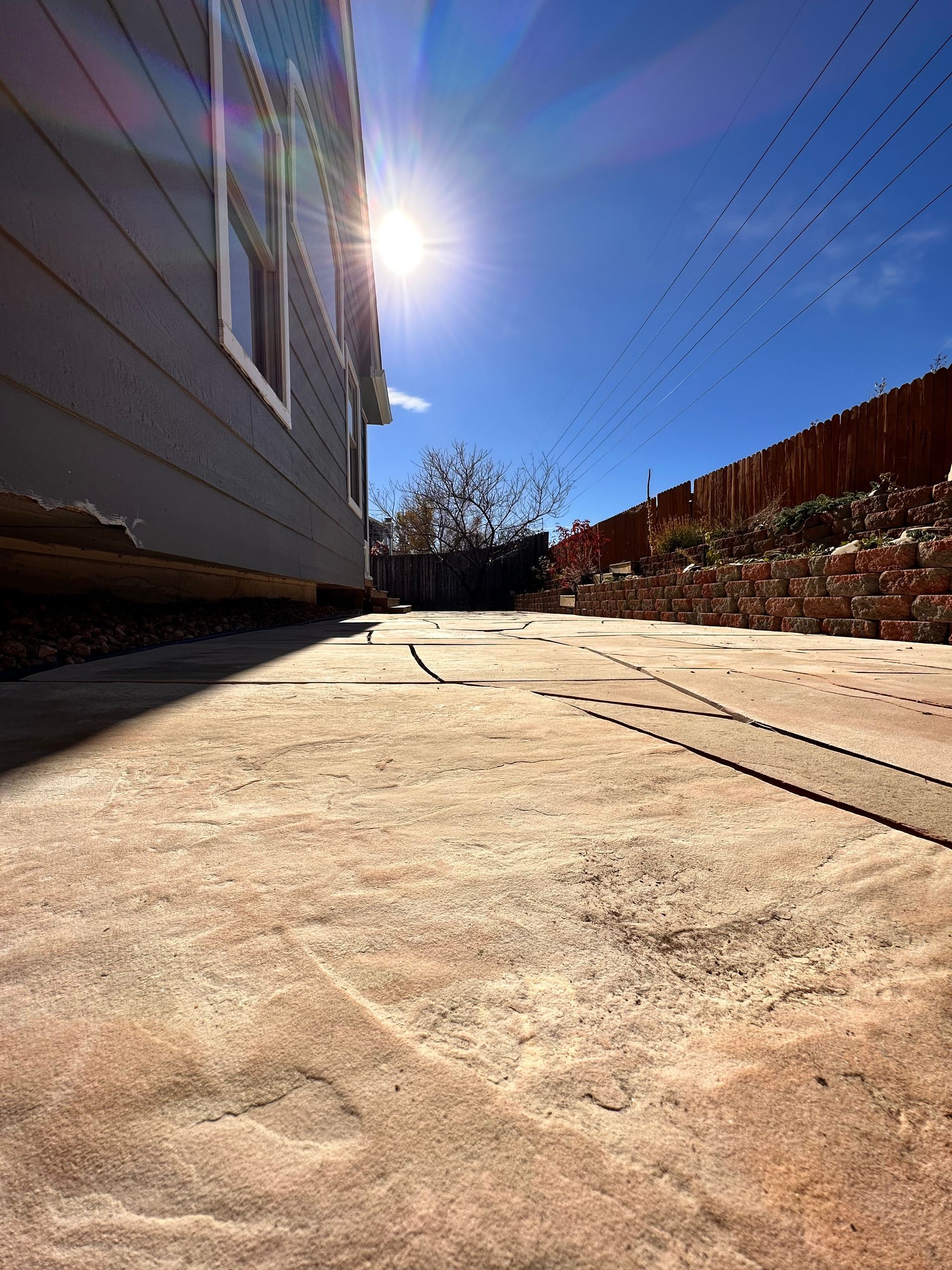 Sunlit stone patio with house and fence; bright blue sky.