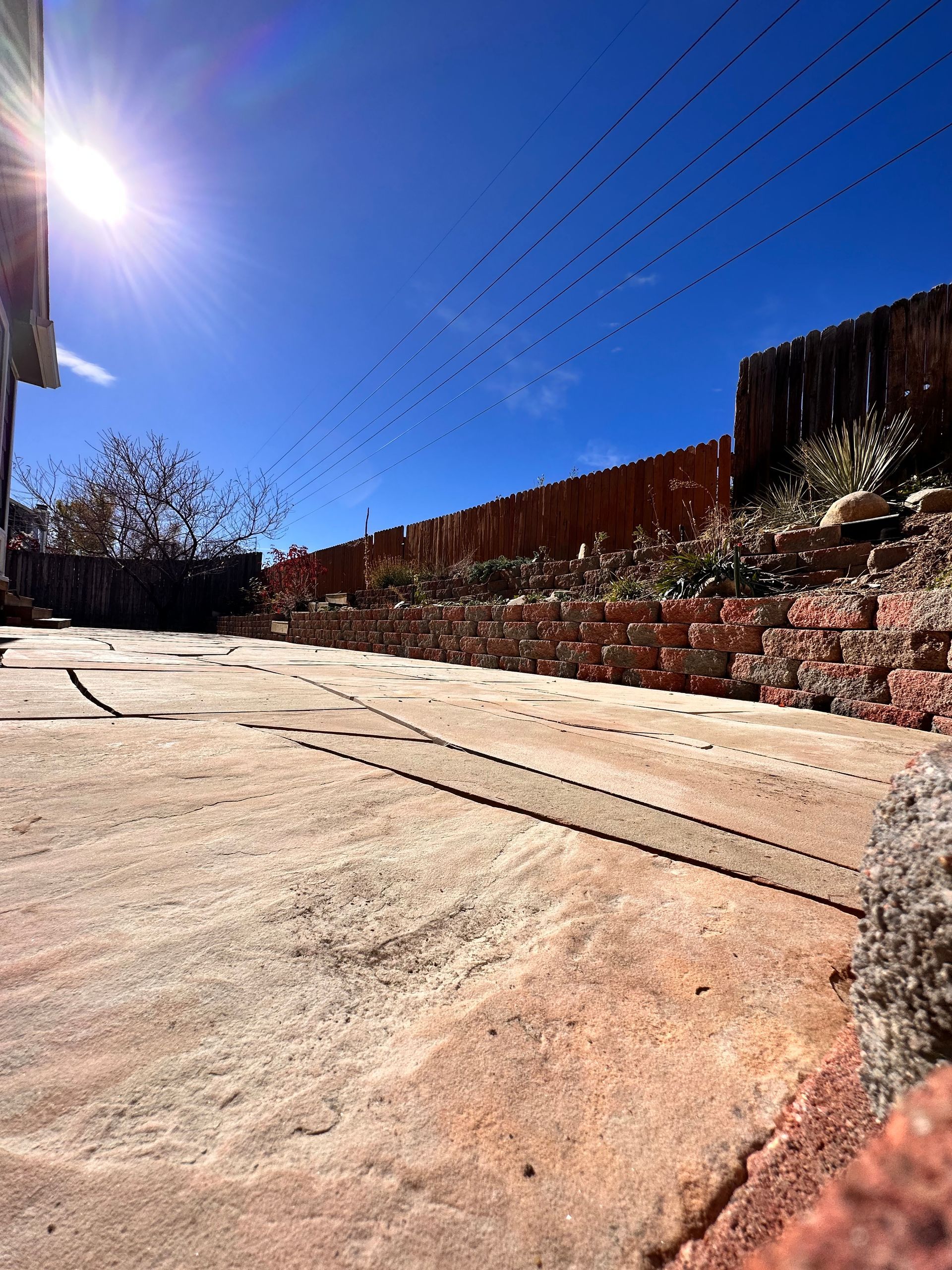 Bright sunny sky over a red brick wall and concrete path; birds fly in the distance.