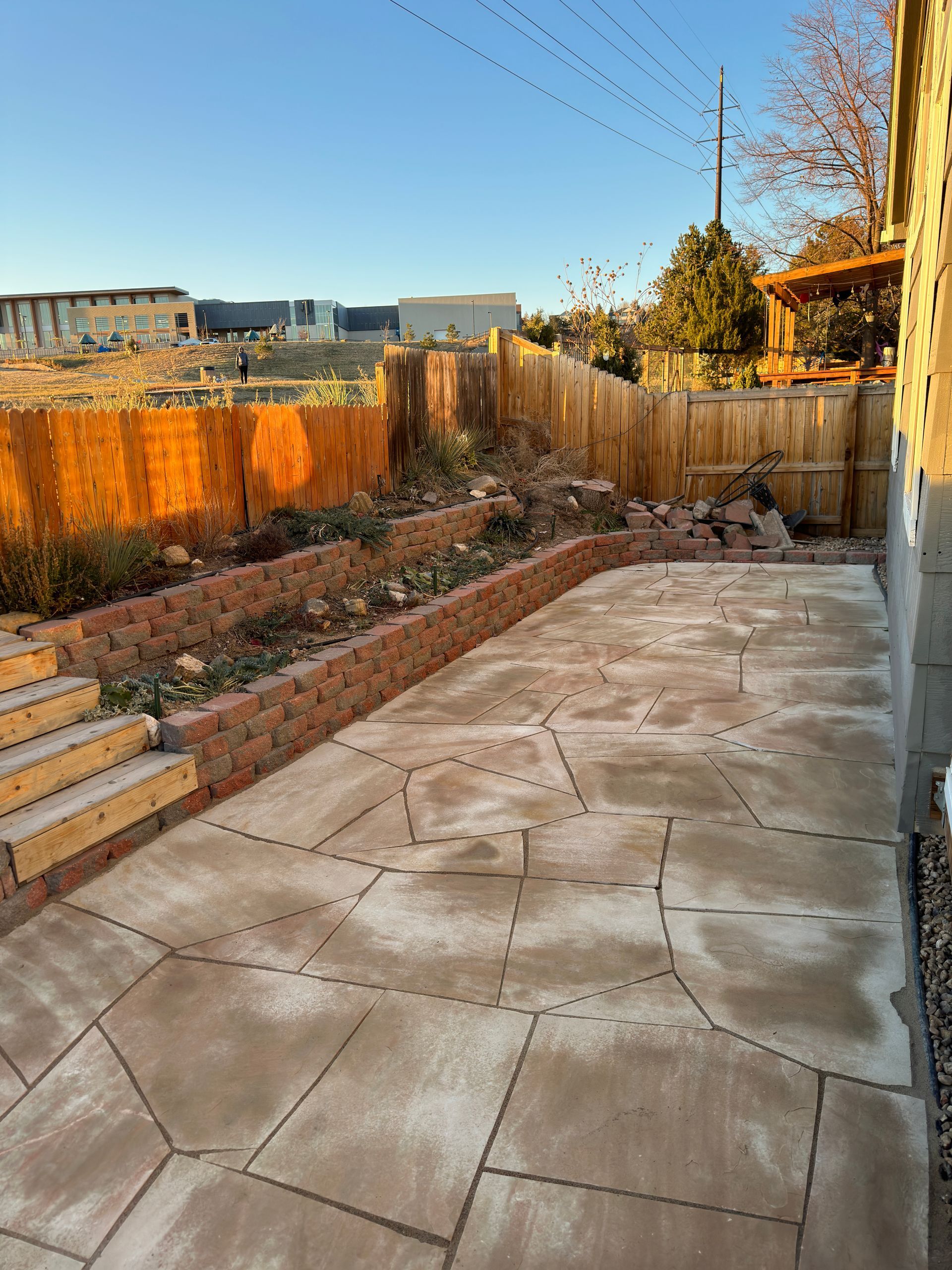 Patio with brick retaining walls, wooden fence, and steps leading to tiered garden beds.