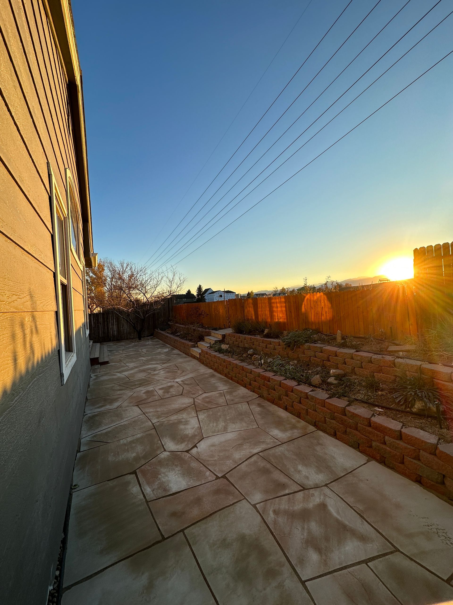 Stone patio with low brick walls, garden beds, and the setting sun.