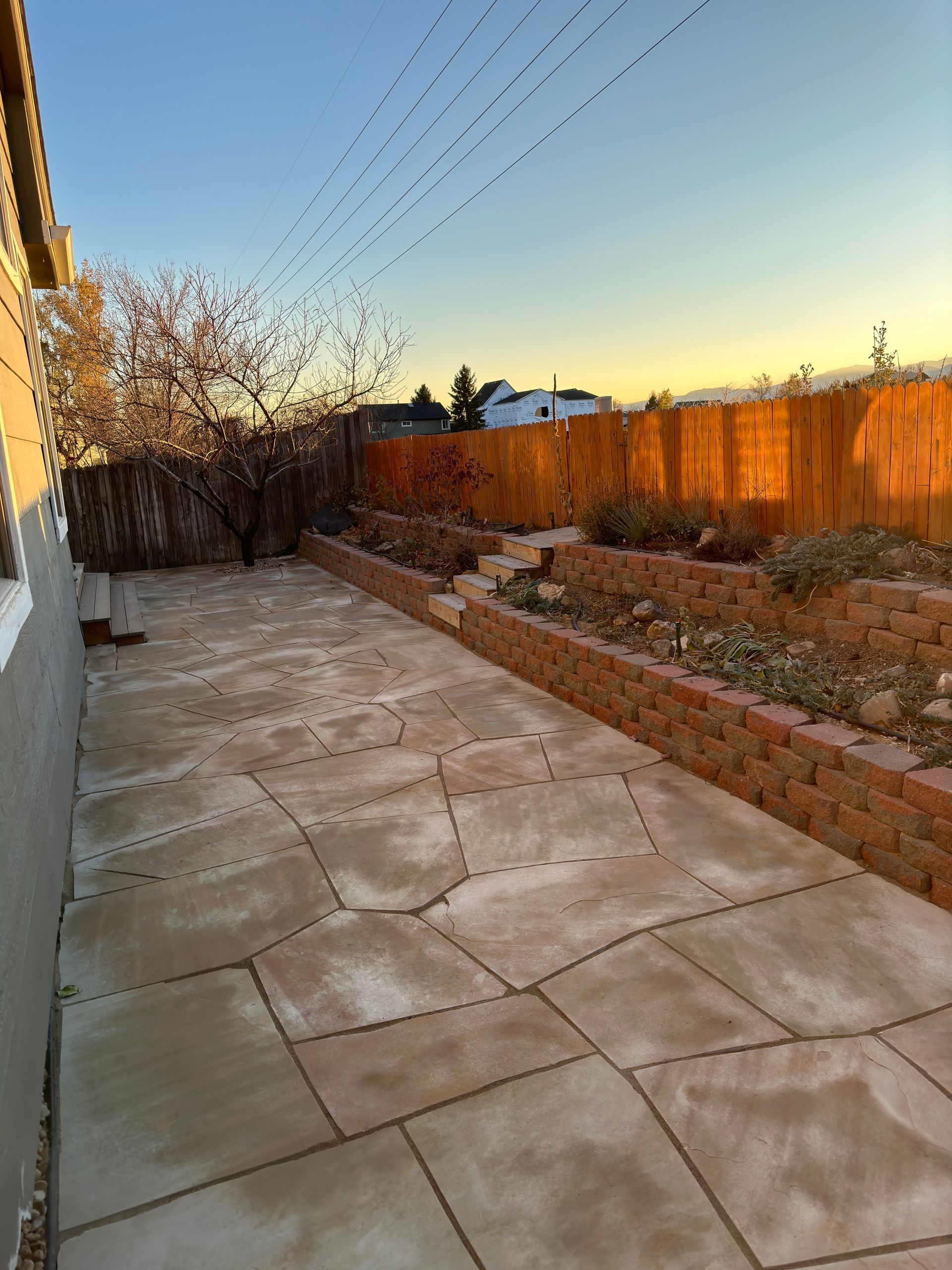 A backyard patio with brick planters and a wooden fence, under a dusk sky.