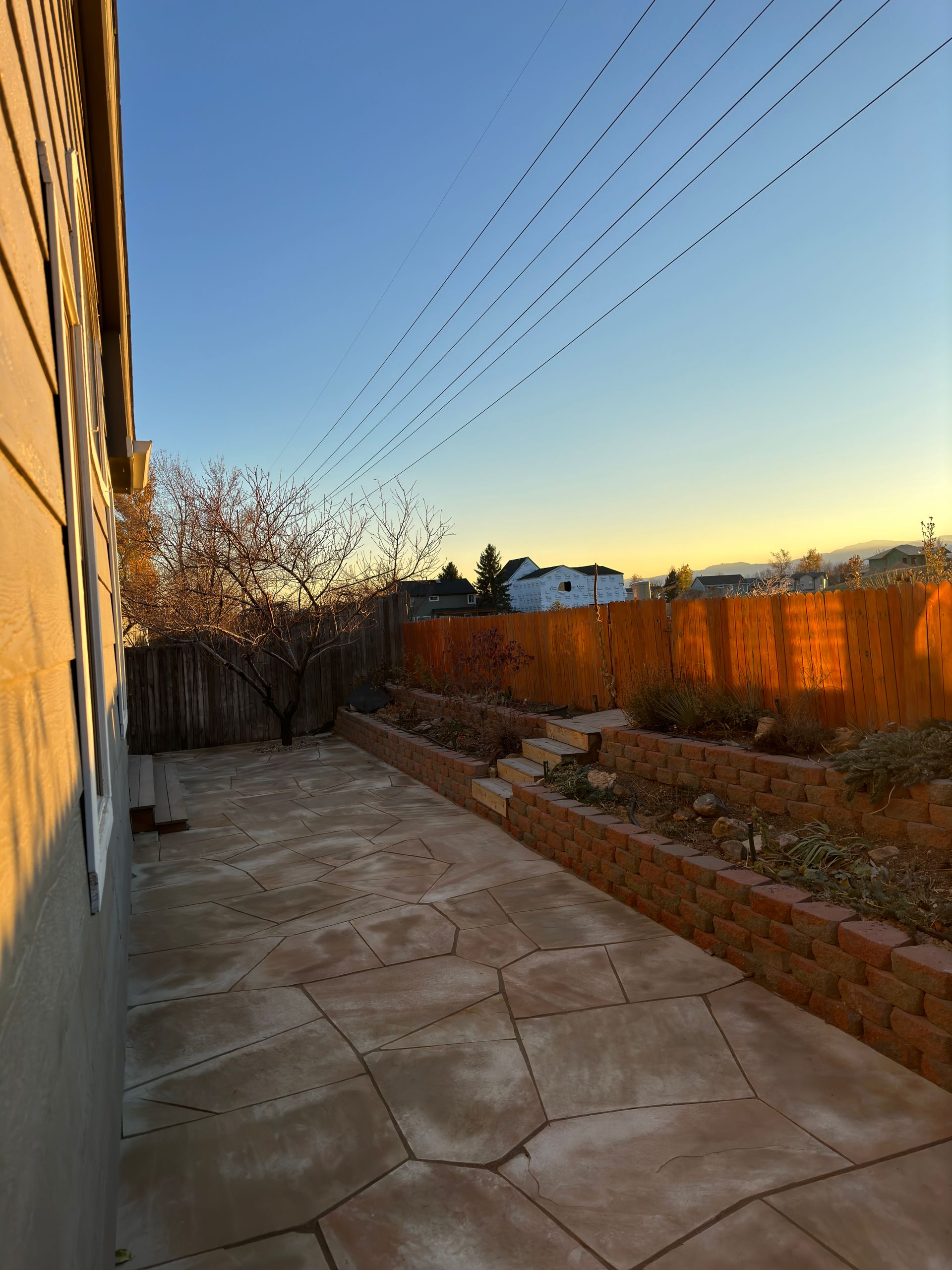 Backyard patio with brick planters, wooden fence, and clear blue sky.